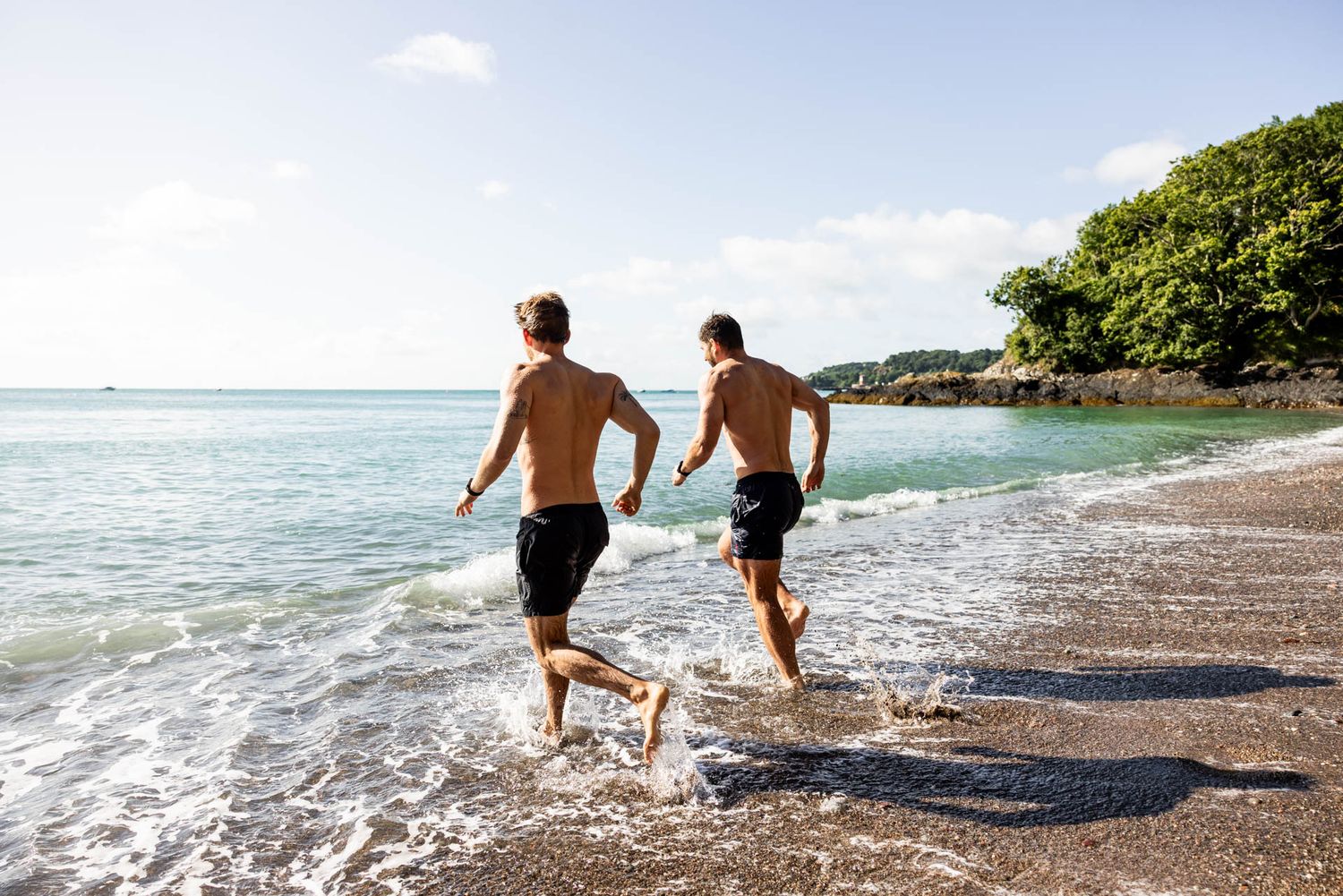 Two people running into ocean waves on tropical beach at sunset.