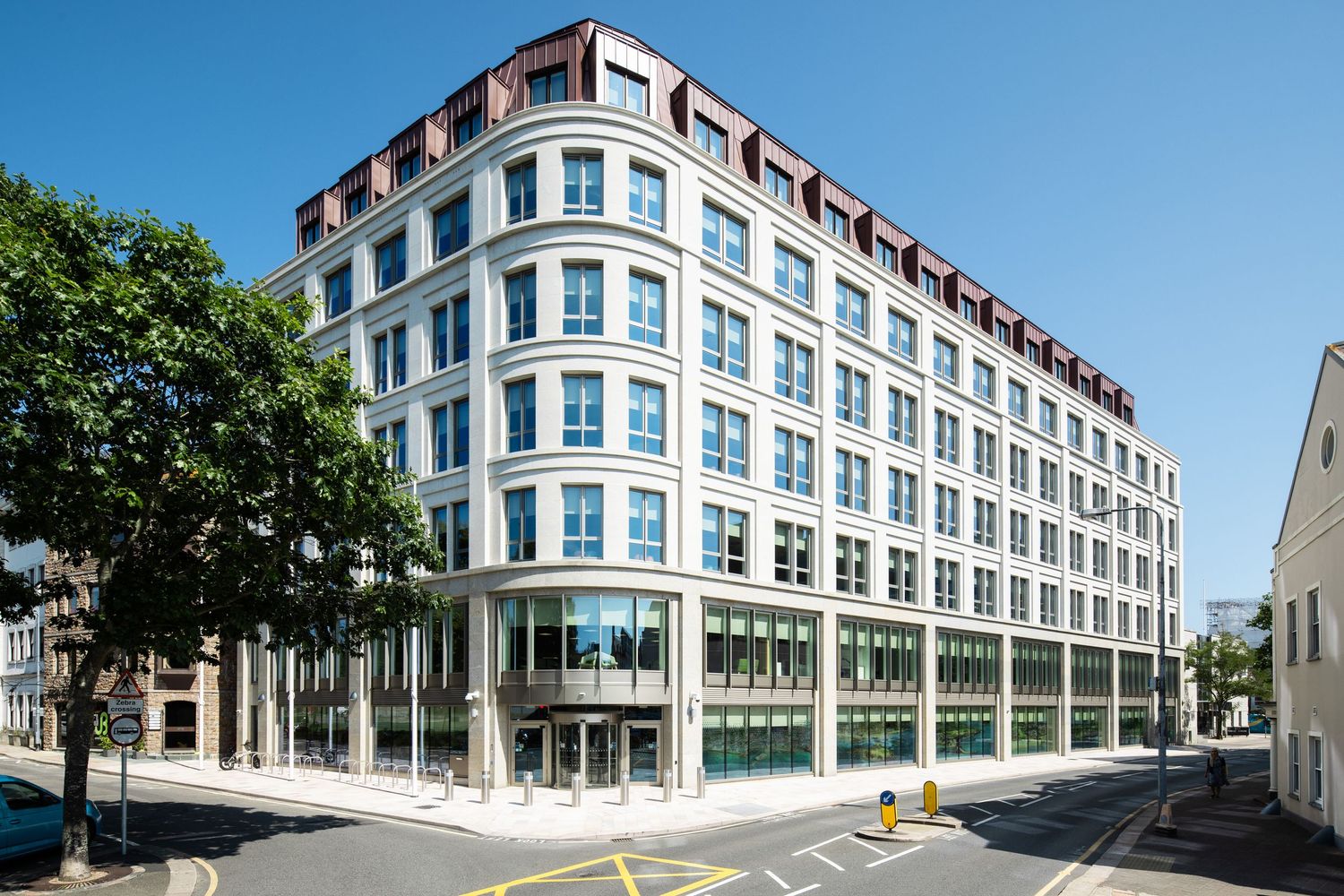 Modern office building with curved blue-tinted windows and white facade on a sunny urban street corner.