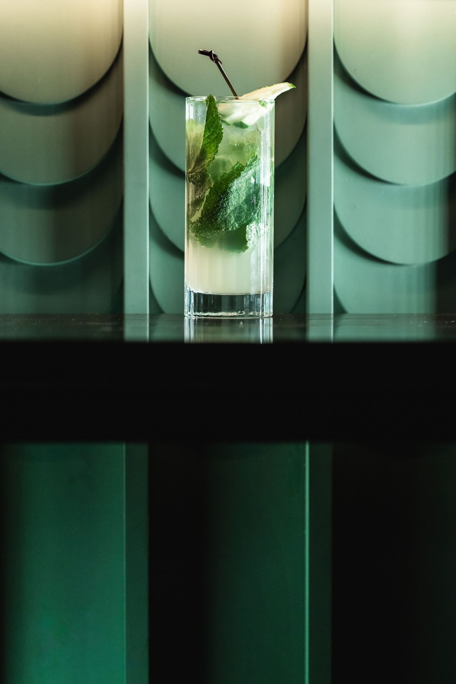 Modern geometric wall design frames an elegant clear cocktail with fresh mint garnish.