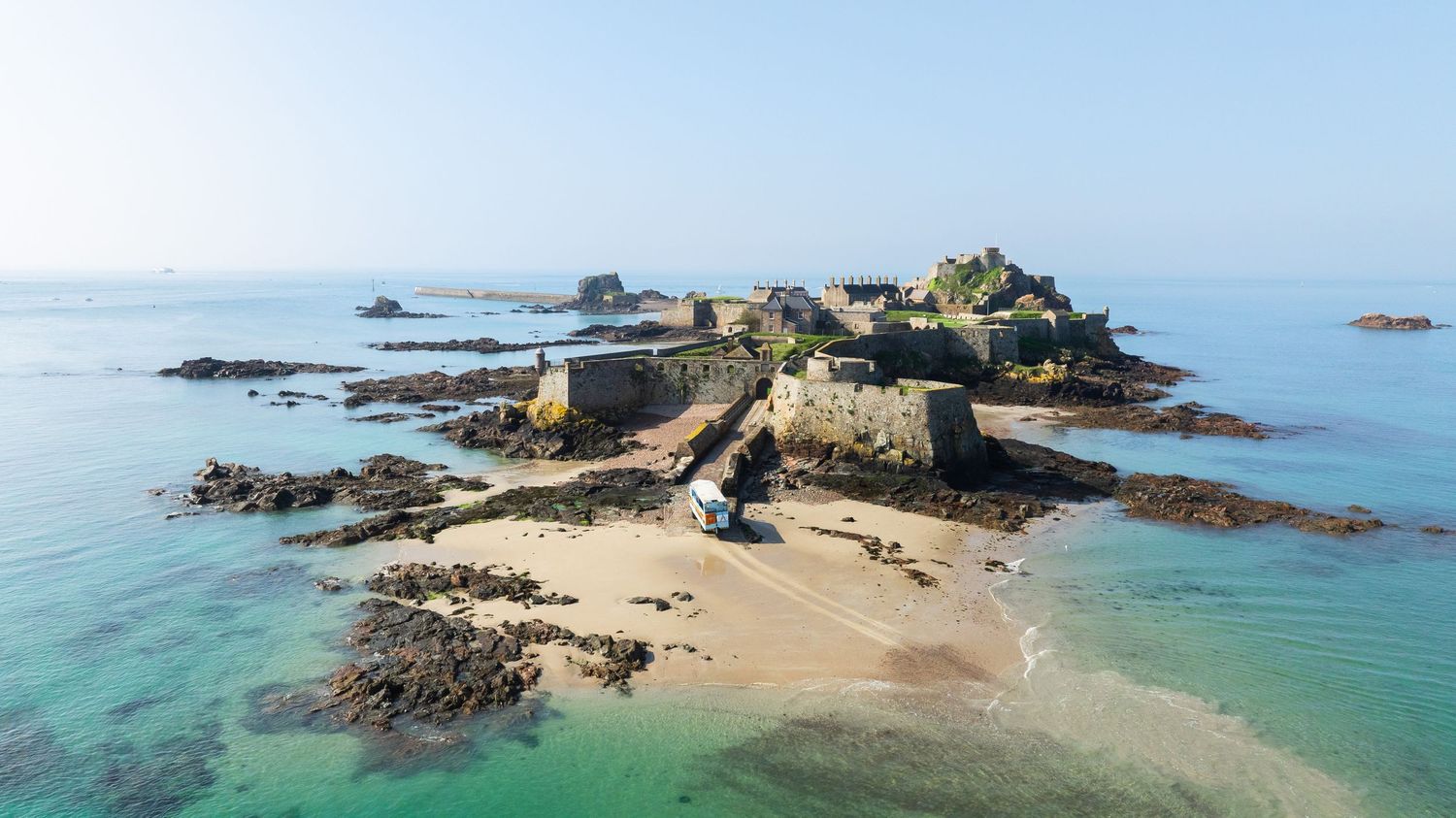 Aerial view of historic fort on rocky island connected by sandy beach path.