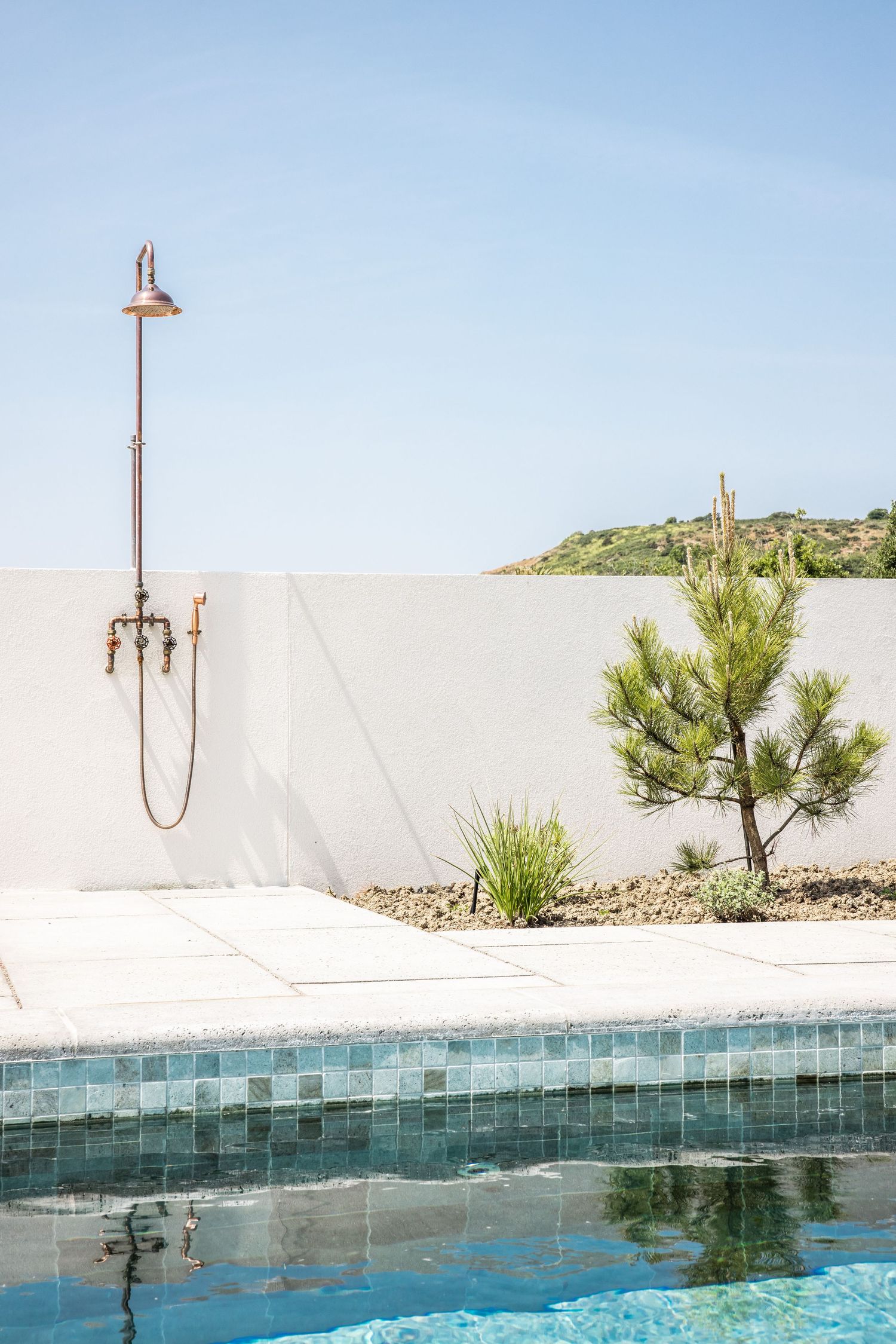 Sleek infinity pool with blue tile detail and outdoor shower against white wall.