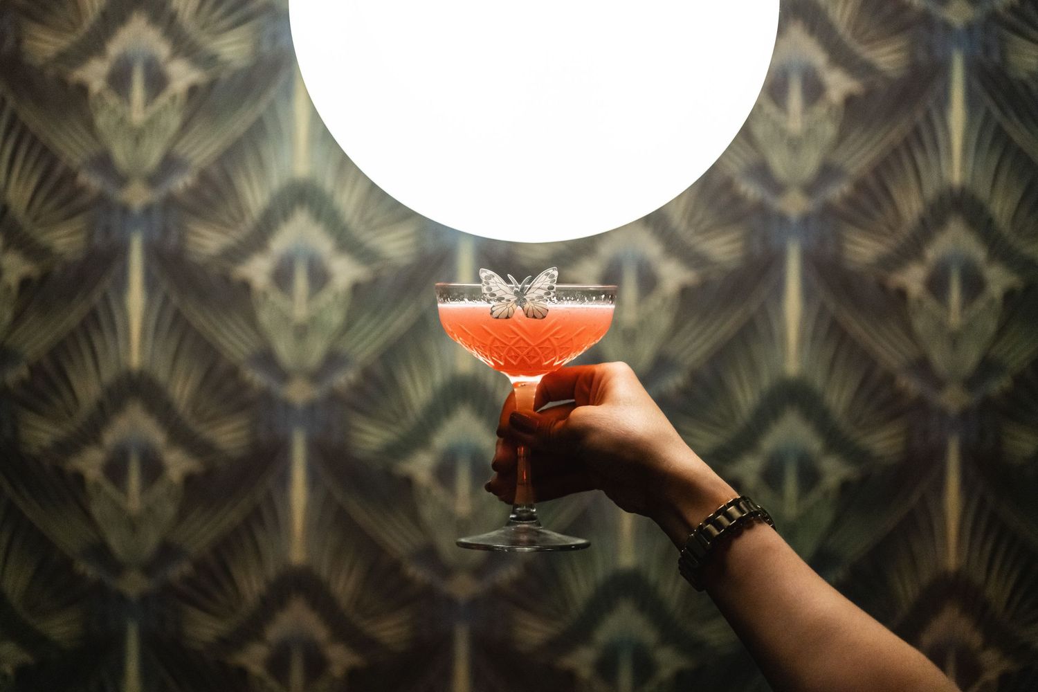 Art deco wallpaper pattern serves as backdrop for sophisticated red cocktail presentation.