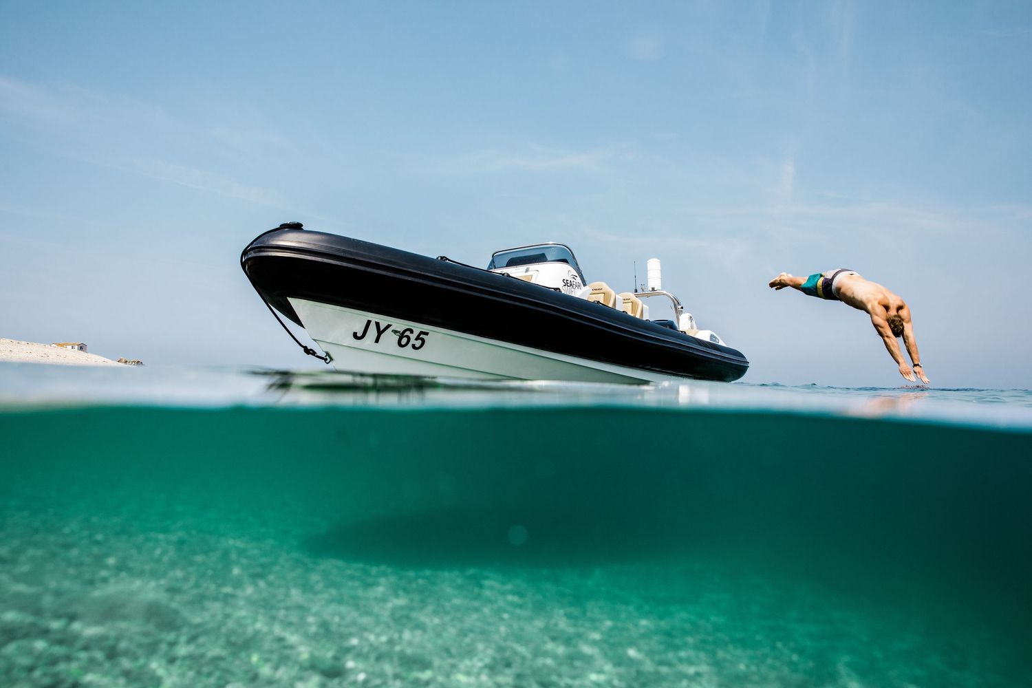 A speedboat jumps over crystal clear turquoise waters as someone dives in from the side.