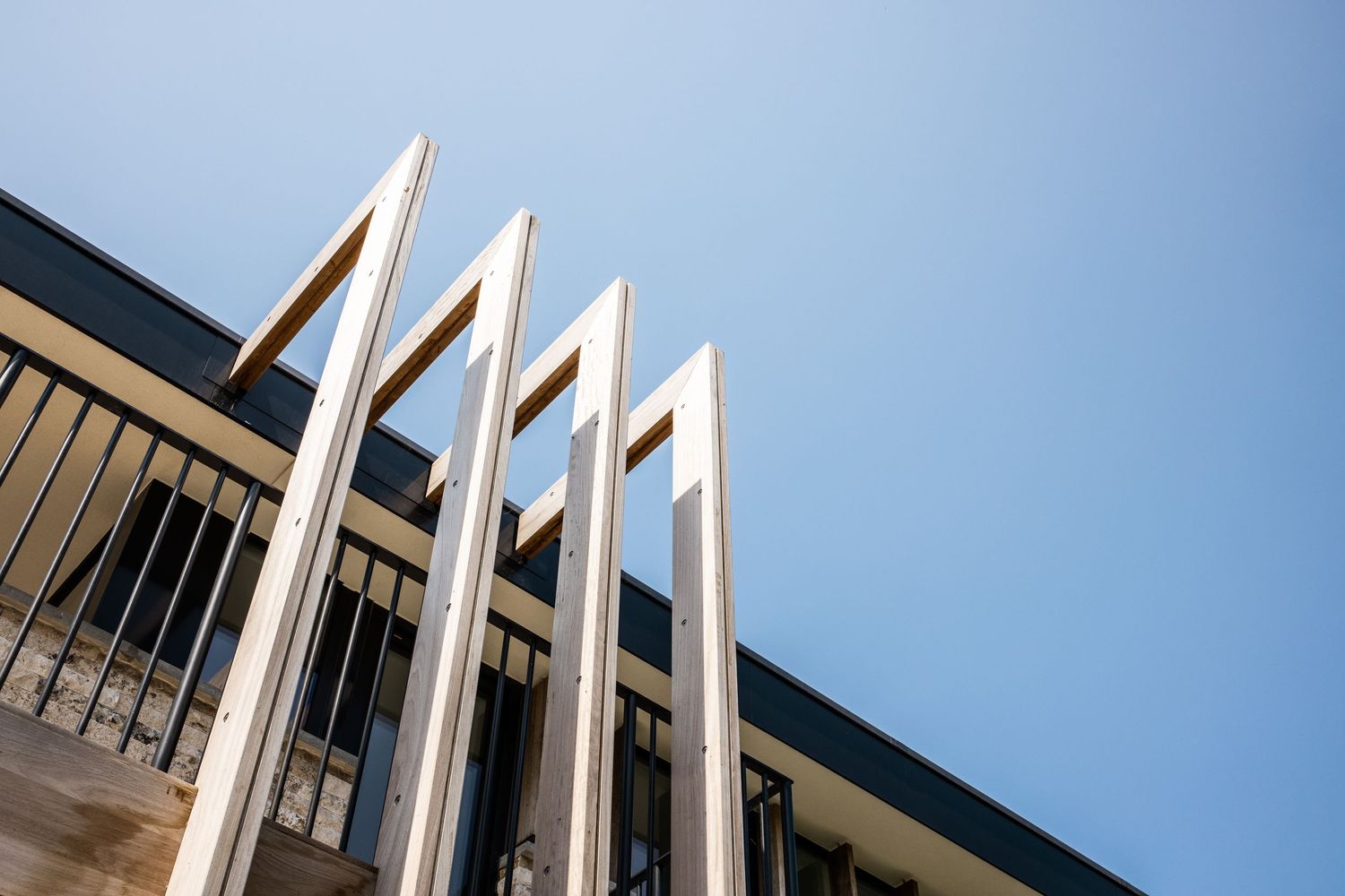 Vertical wooden beams create geometric patterns against modern building's glass facade.
