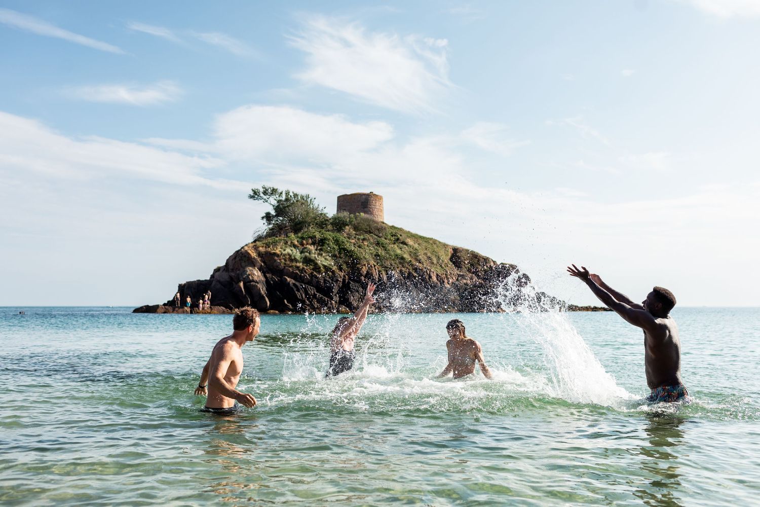 Group enjoying a playful swim in crystal clear ocean waters on a sunny summer day.