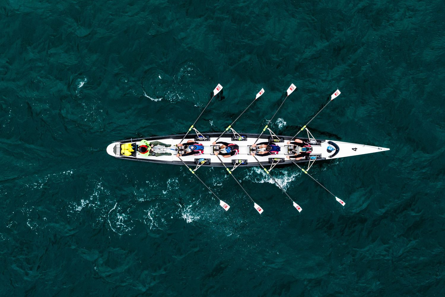 Aerial view of rowing team practicing in dark teal waters.