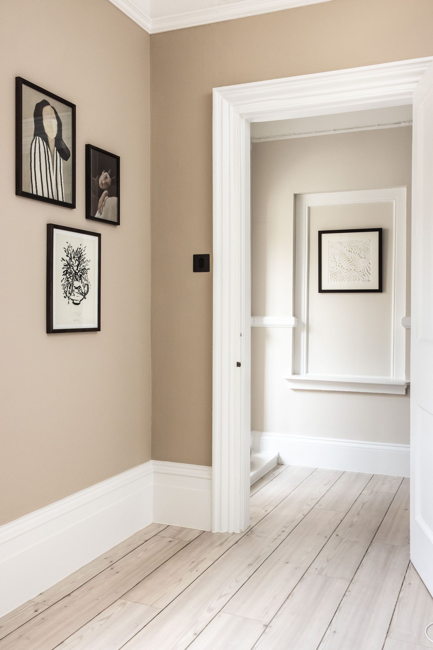 Minimalist interior hallway with white painted floors and beige walls featuring black framed artwork.