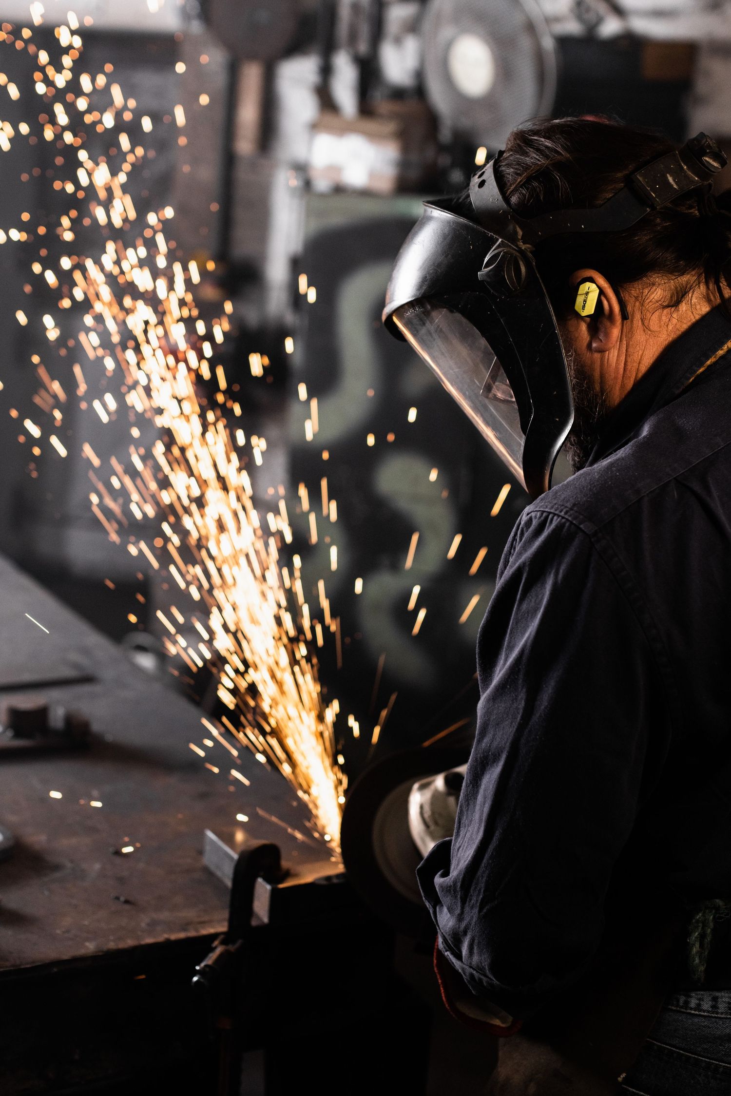 Welder in protective gear working with sparks flying in industrial setting.