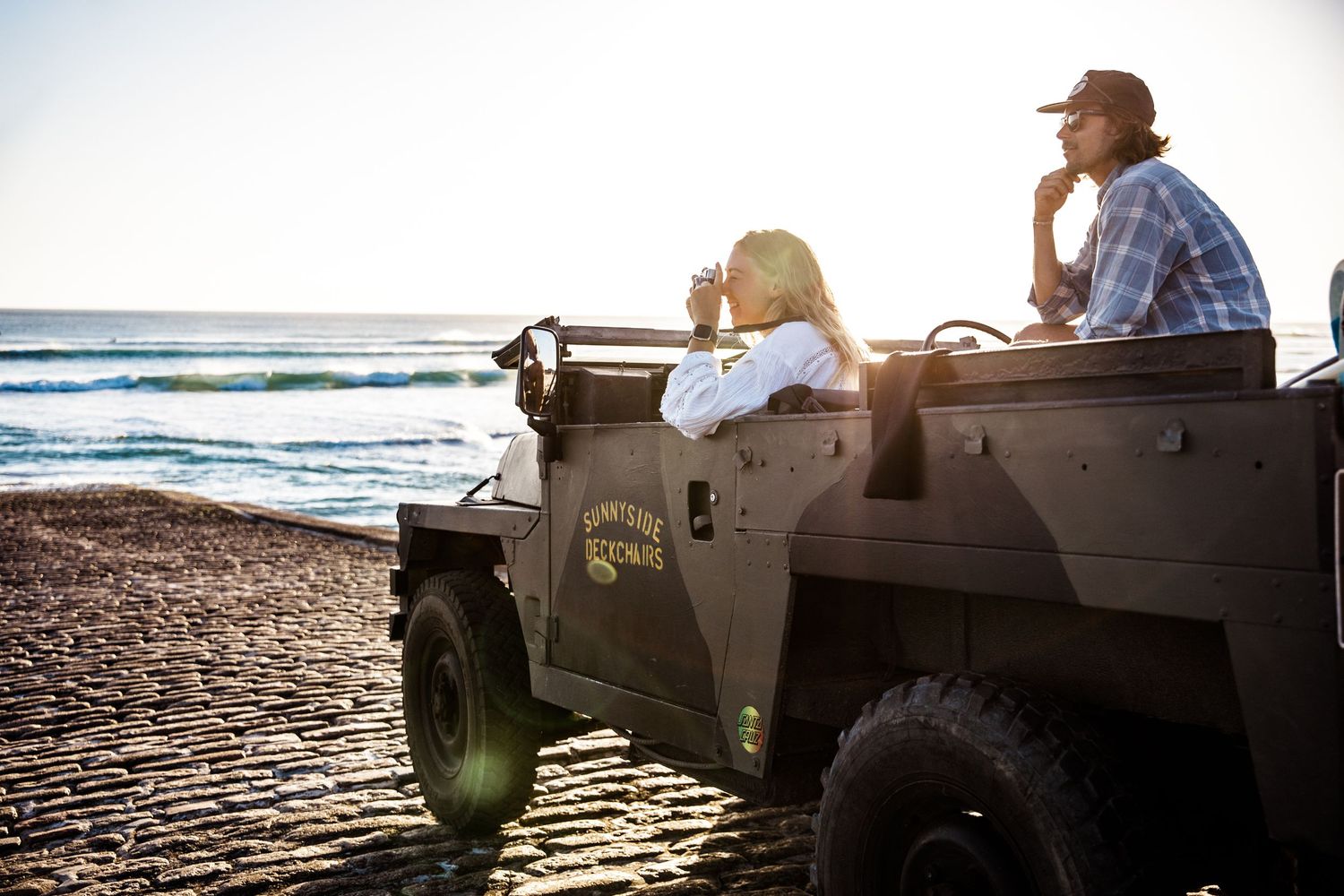 Off-road vehicle parked on a beach at sunset with ocean waves in the background.