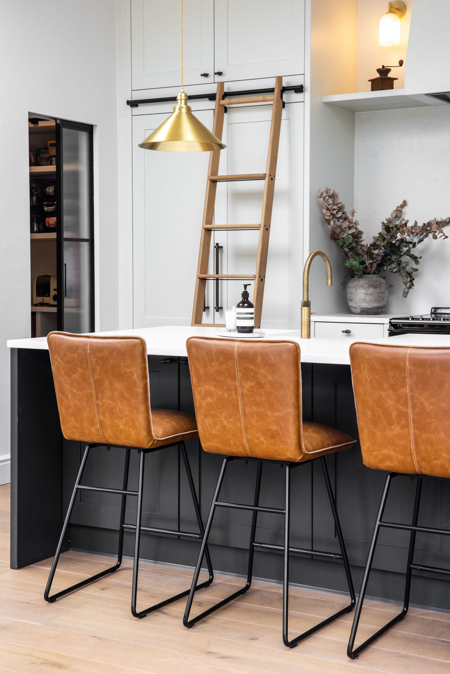 Modern kitchen island with brown leather bar stools and brass pendant lighting creates a sleek dining space.