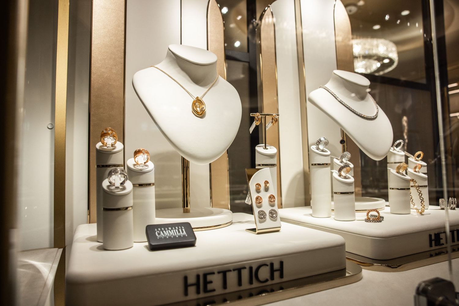 Elegant jewelry display featuring necklaces on white stands in a Hettich store window.