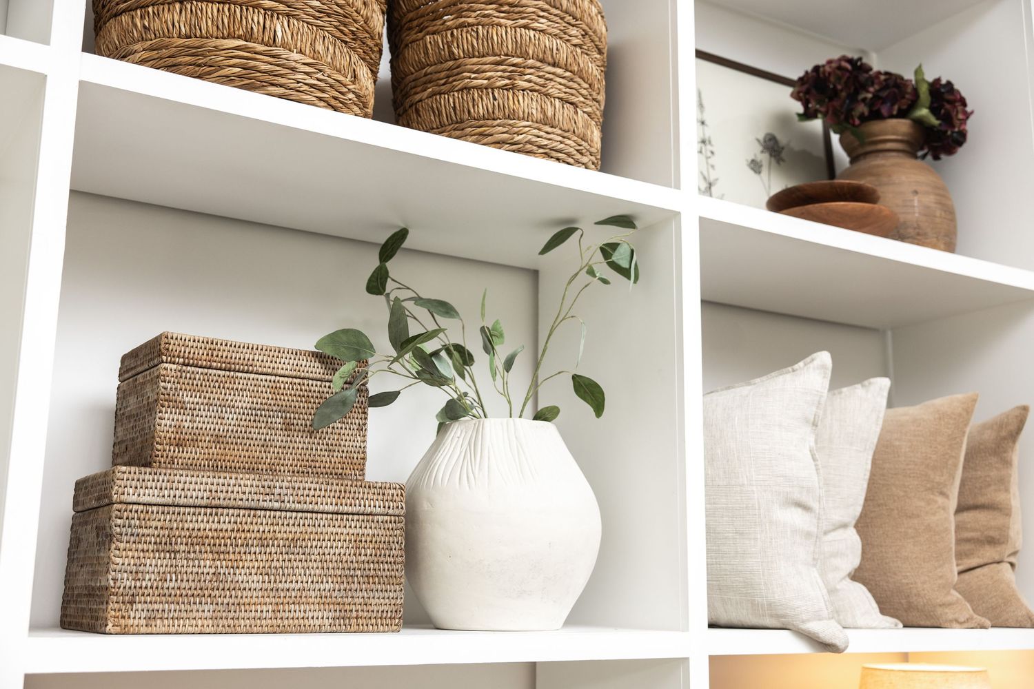 Organized white shelving unit displaying woven baskets and decorative items in neutral tones.
