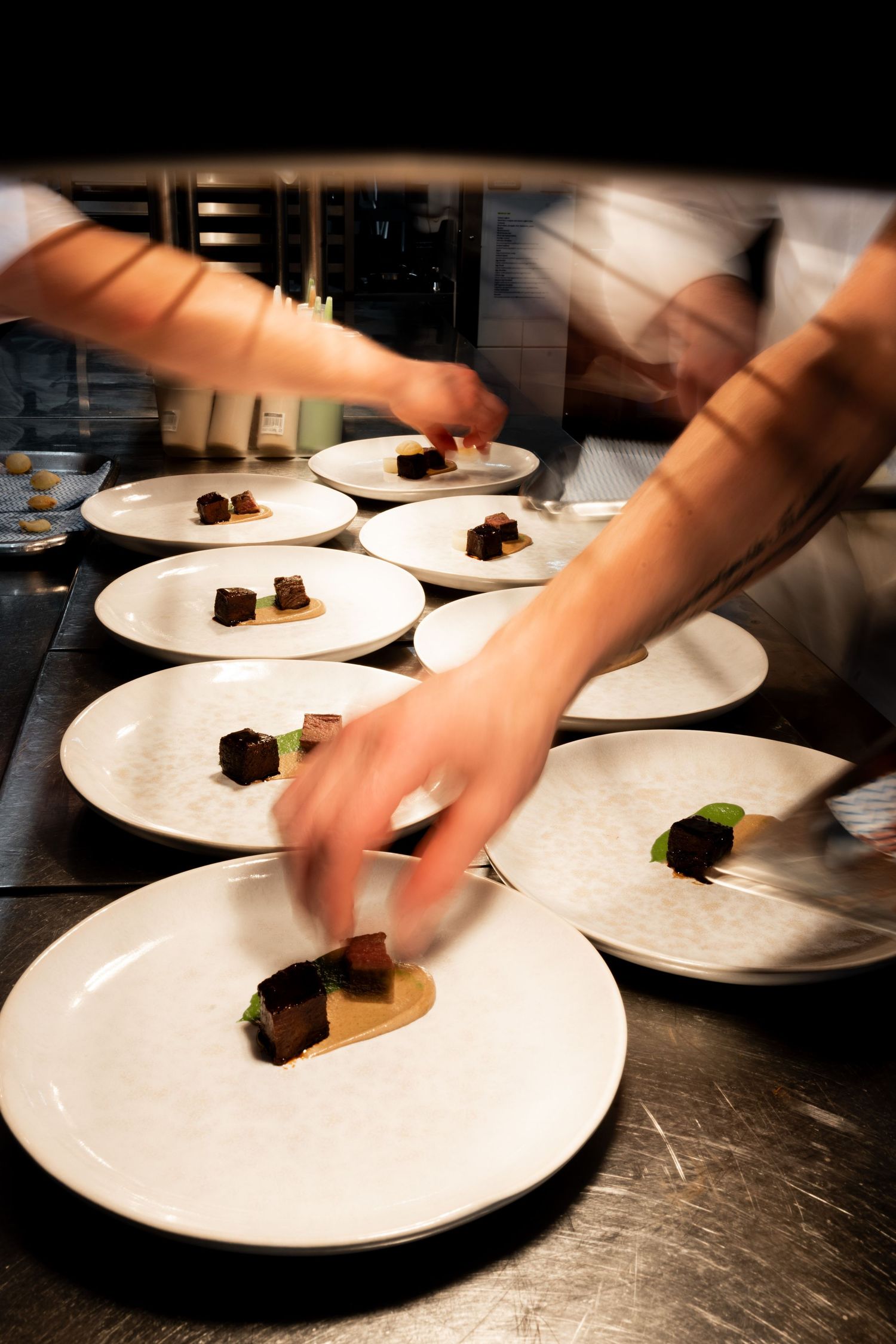 Multiple white plates being prepared simultaneously in restaurant kitchen.