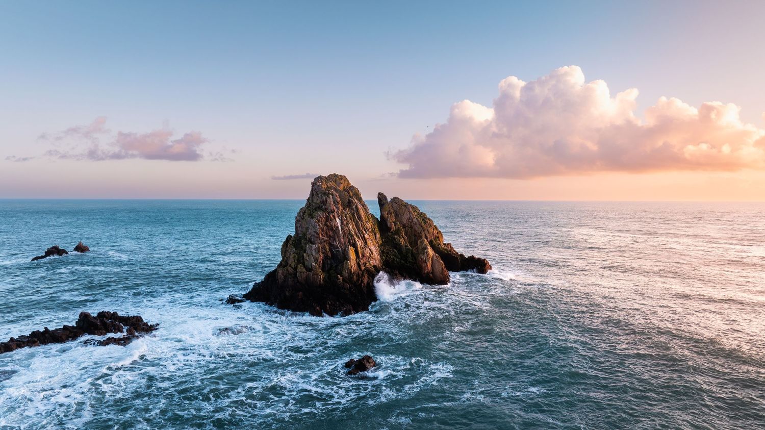 Serene sunset panorama over the ocean horizon with soft pink clouds and calm waters.