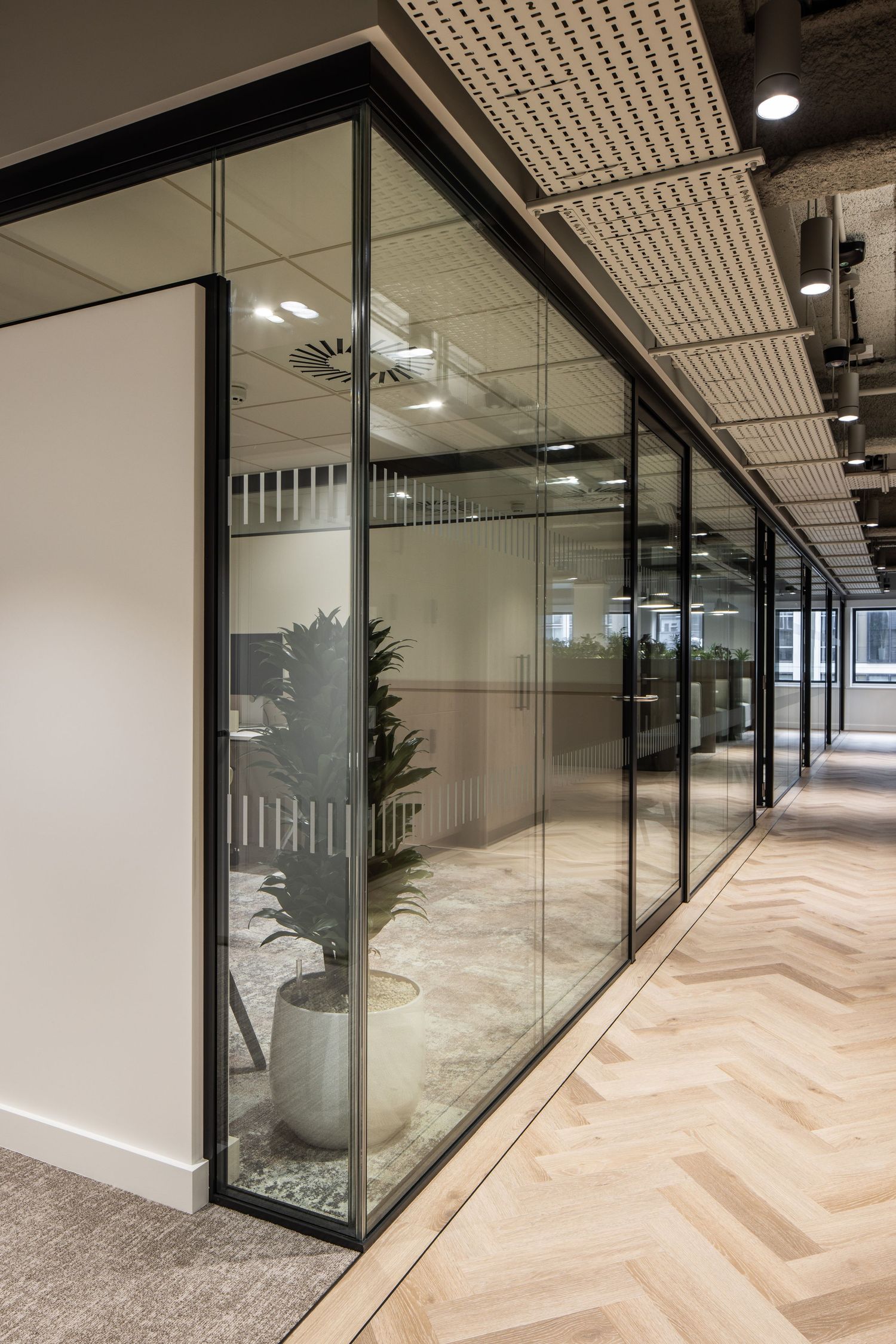 Corporate hallway with glass partitions, herringbone flooring, and modern architectural details.
