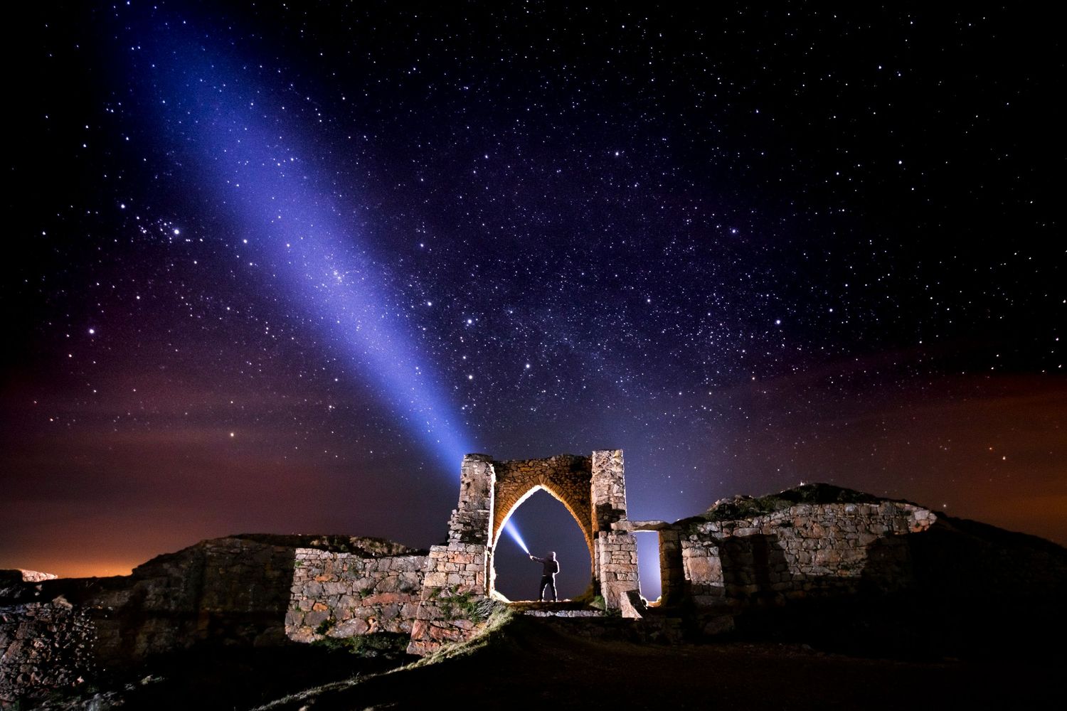 Blue light beam illuminating ancient ruins against starry night sky.