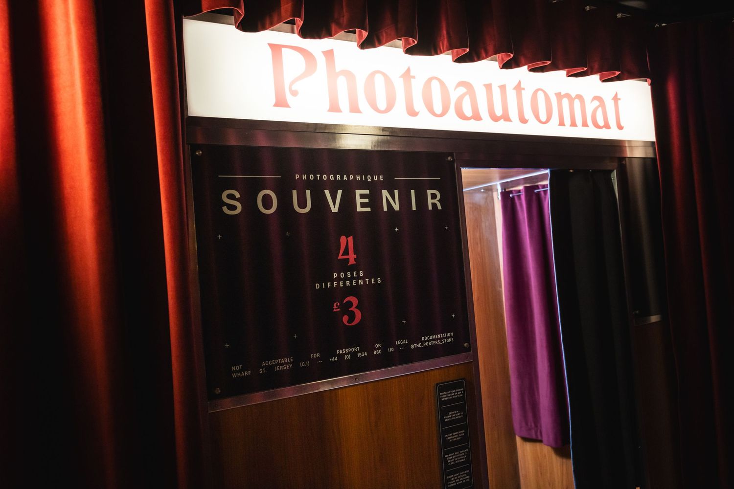 Vintage style photoautomat souvenir booth with red curtains and illuminated signage.