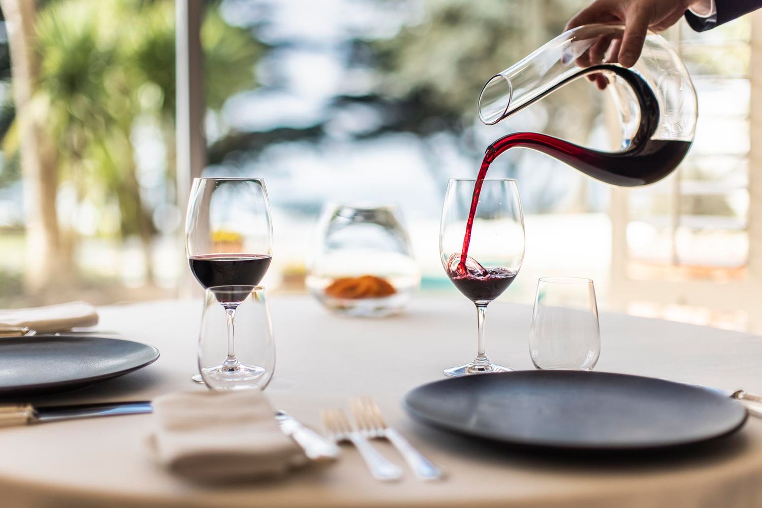 Red wine being poured into a glass at an elegant dining table setting.
