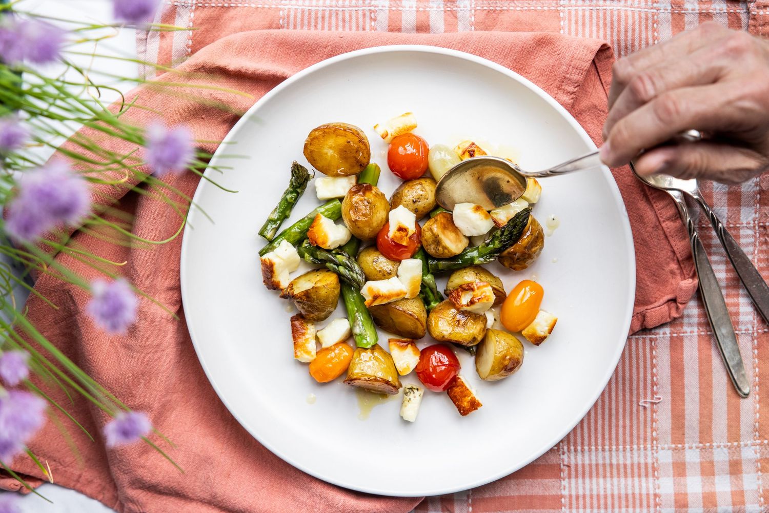 Roasted potatoes with fresh herbs and vegetables arranged on white plates.