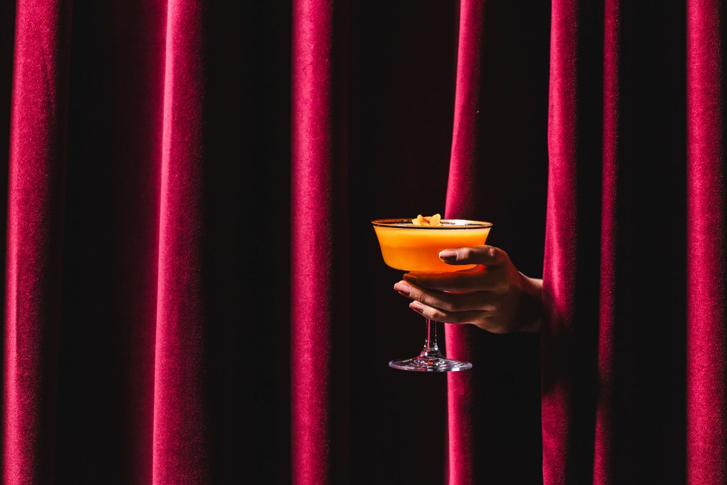 Red velvet curtains provide dramatic backdrop for elegant cocktail service in upscale bar setting.
