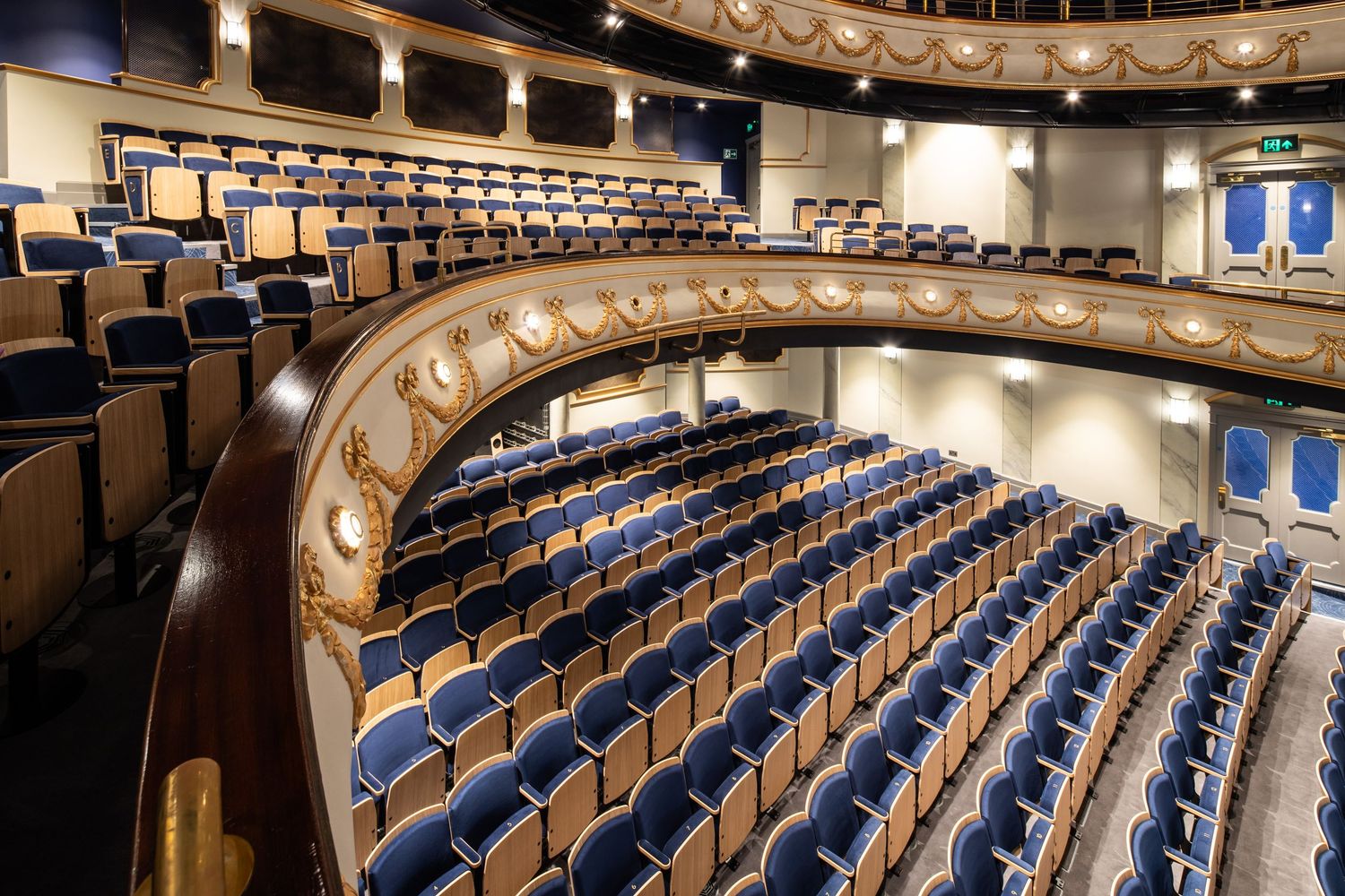 Interior view of a modern theater auditorium with curved rows of blue seats and ornate architectural details.