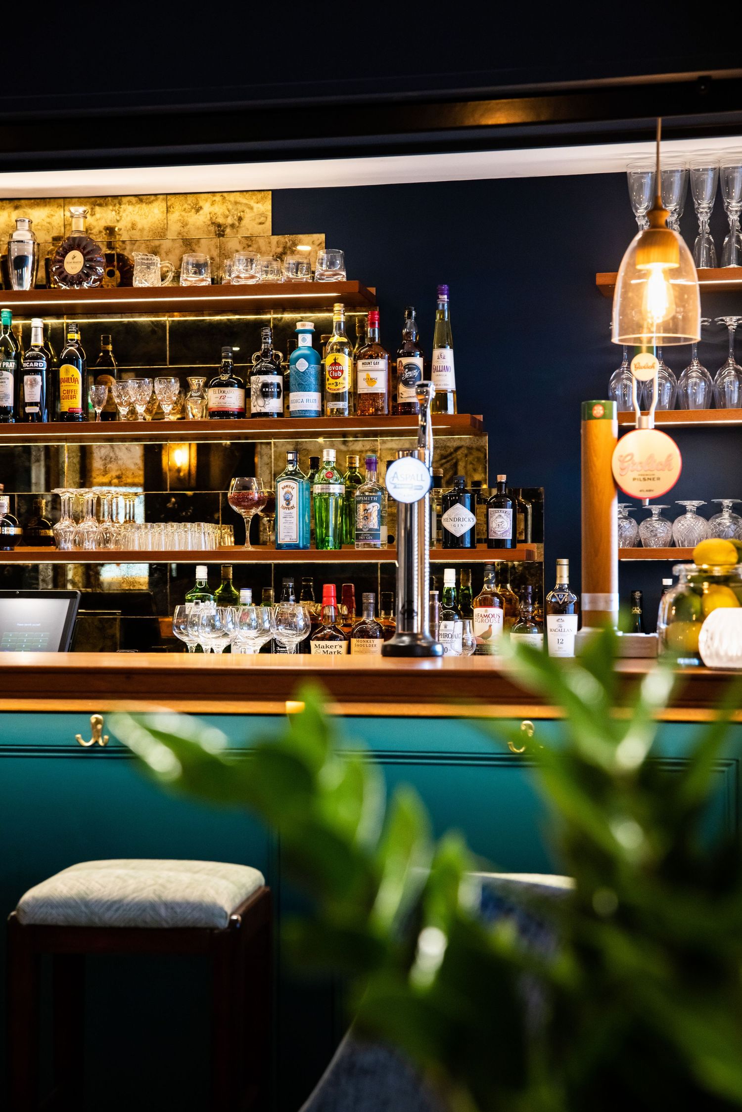 Modern bar interior with illuminated shelving displaying liquor bottles against a dark blue wall.