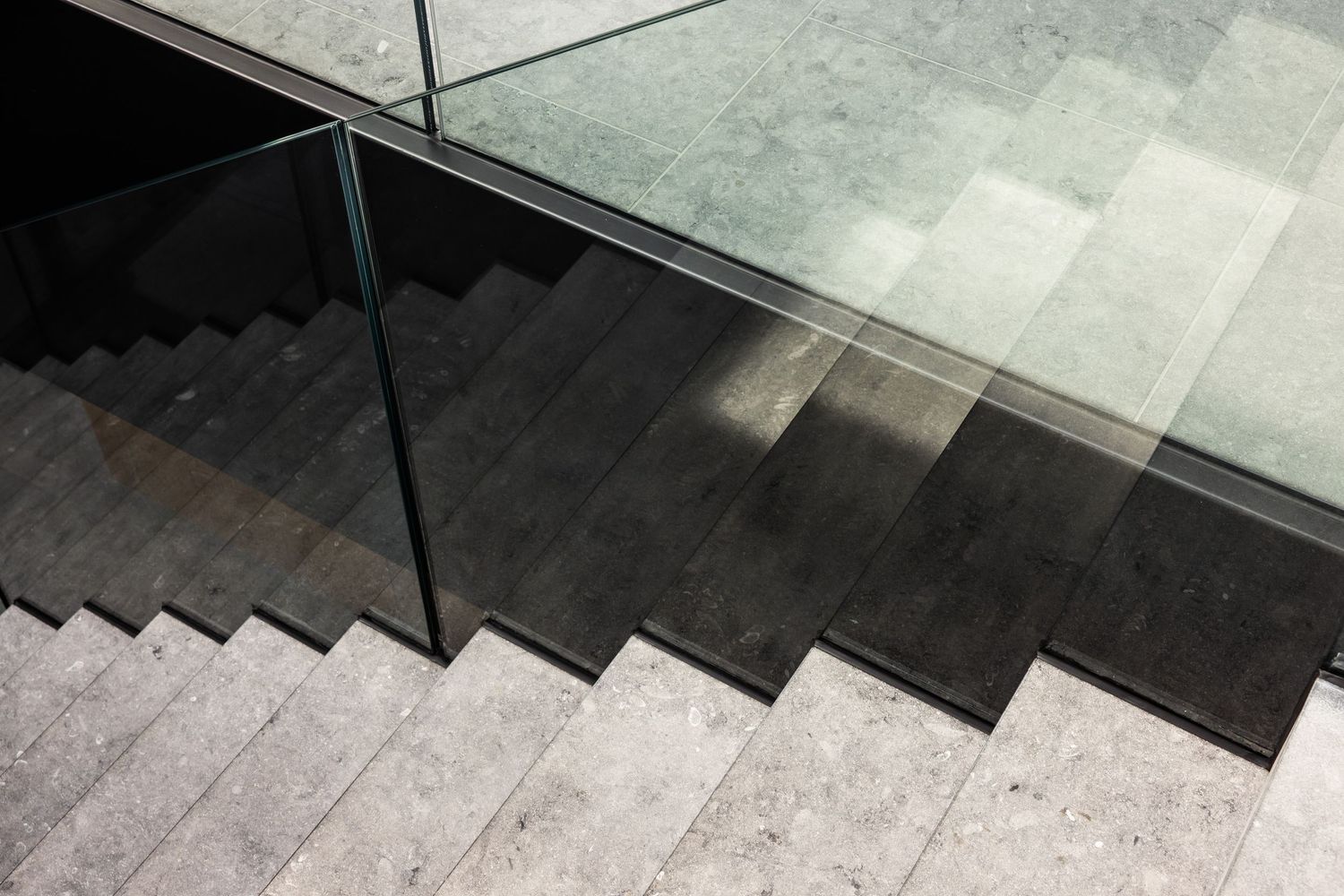 Modern black stone staircase with glass railing and dramatic lighting.