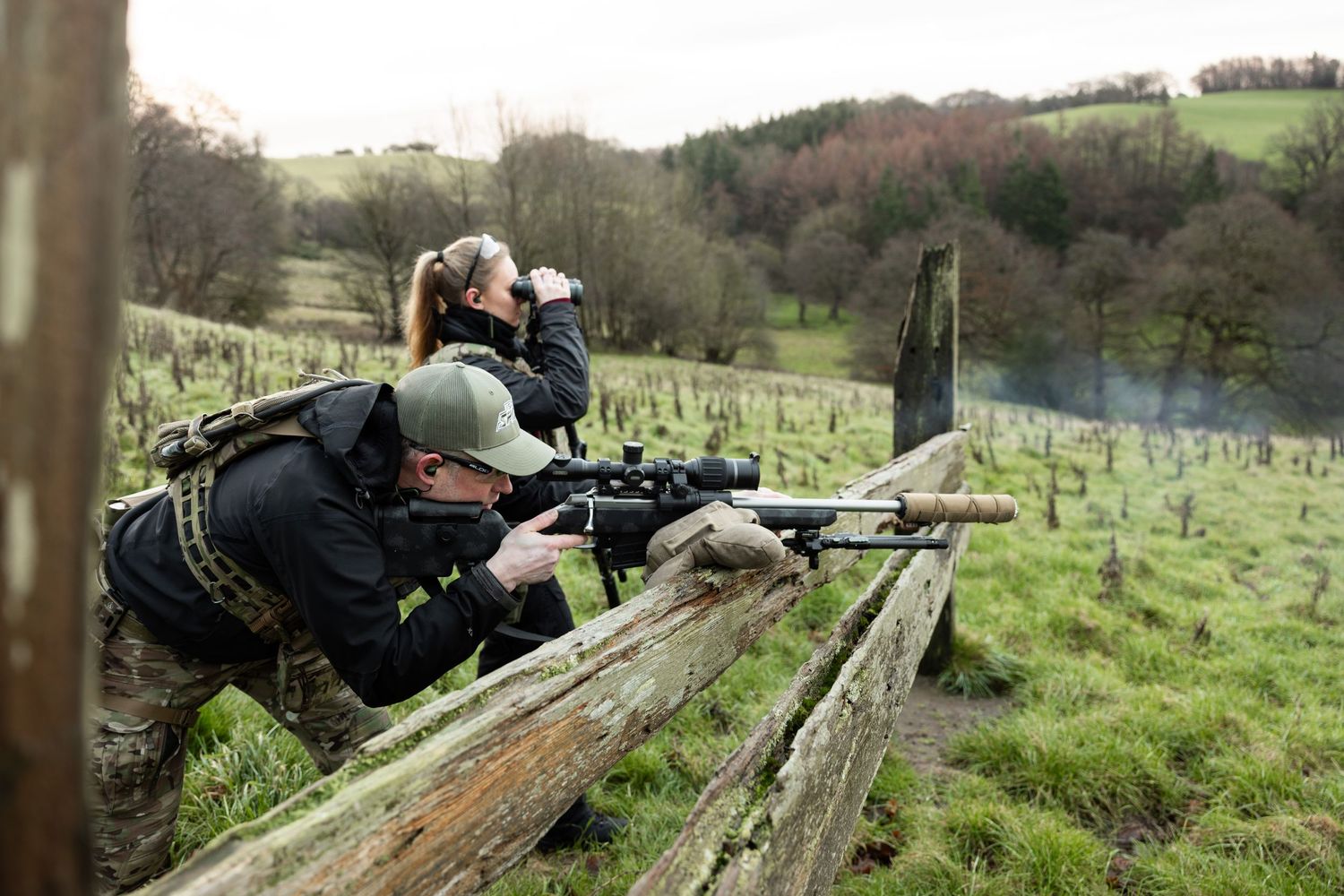 People practicing long-range shooting at an outdoor range in rural terrain.
