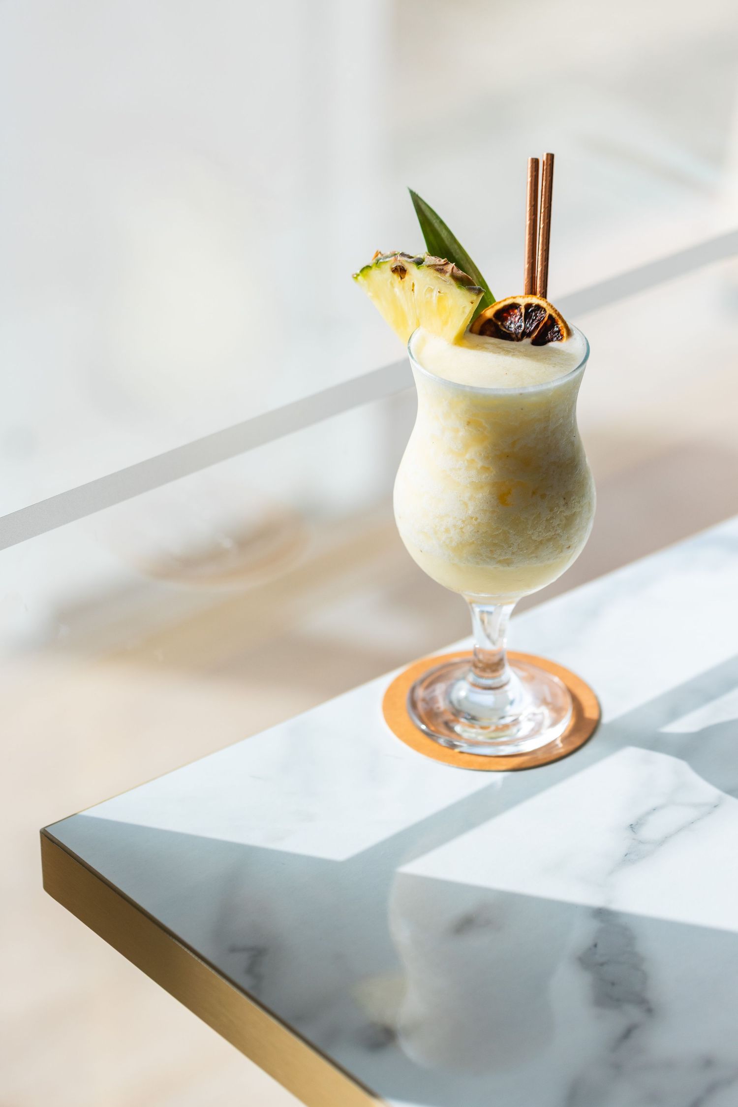 Series of tropical cocktails with pineapple garnish served in stemmed glasses on a marble surface.