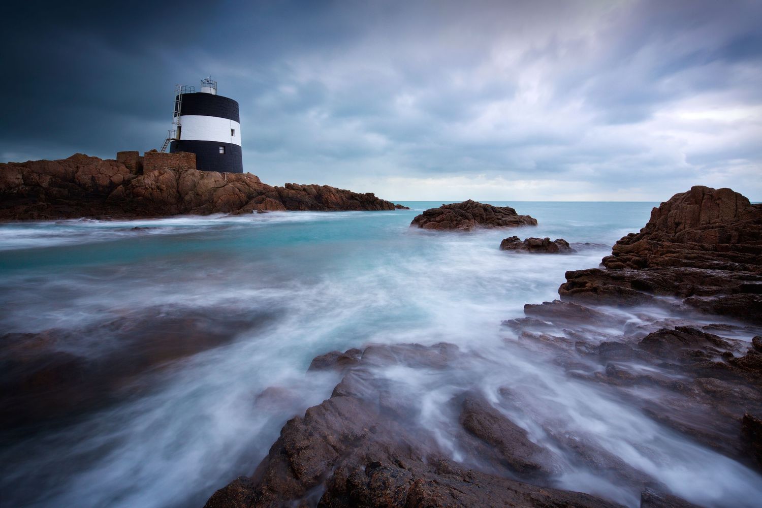 Long exposure seascape showing dramatic waves and rocky coastline under stormy skies.