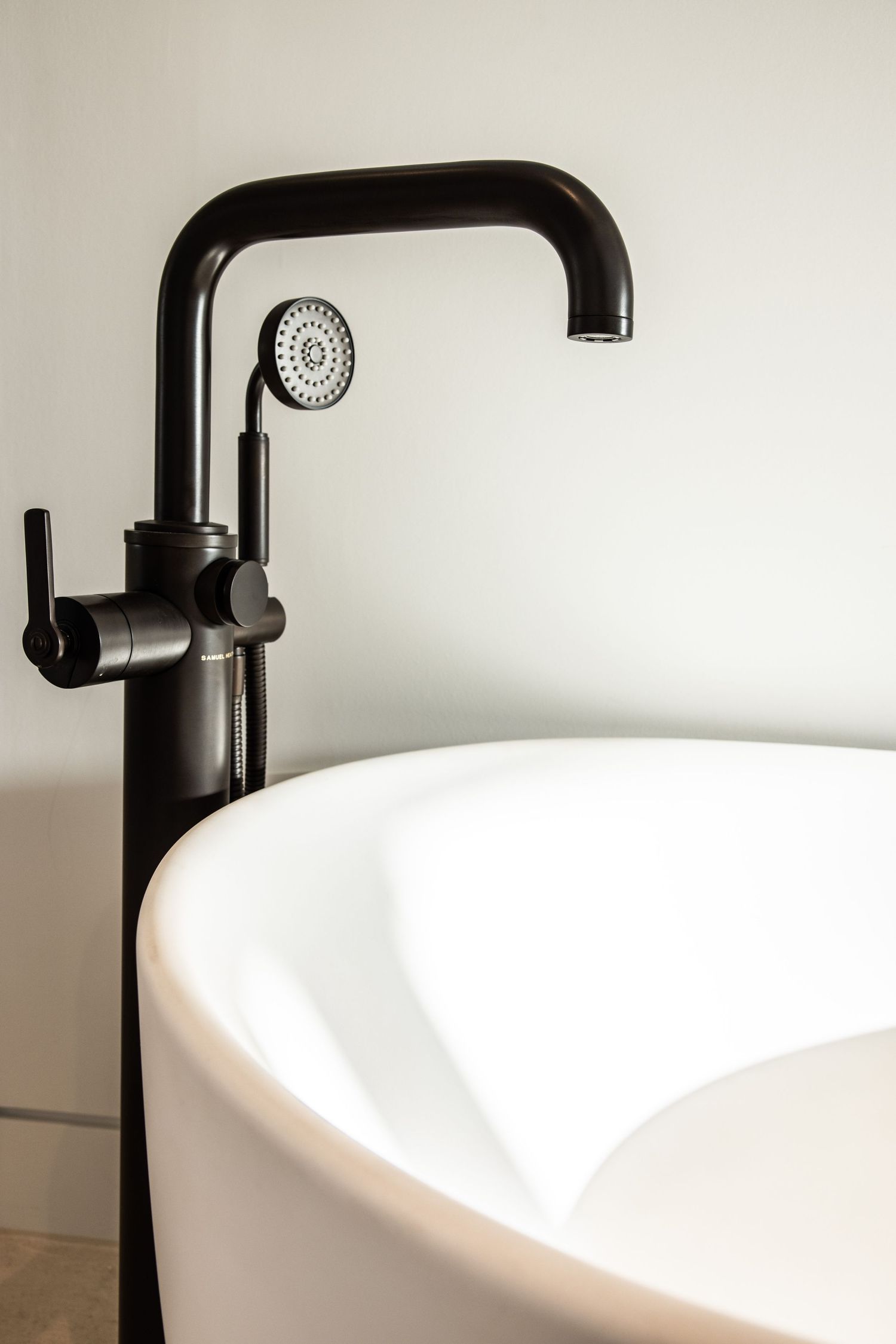 Modern matte black faucet fixture beside white freestanding bathtub.