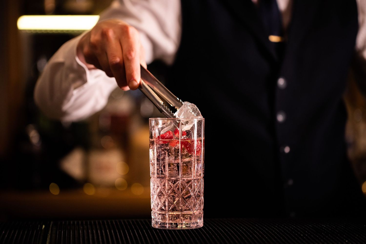 Close-up of hands pouring cocktails into crystal glasses at upscale bar.