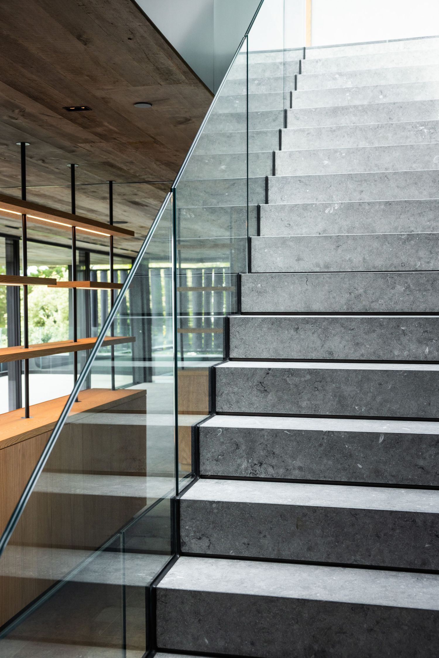 Contemporary concrete staircase with glass balustrade and wooden ceiling detail.