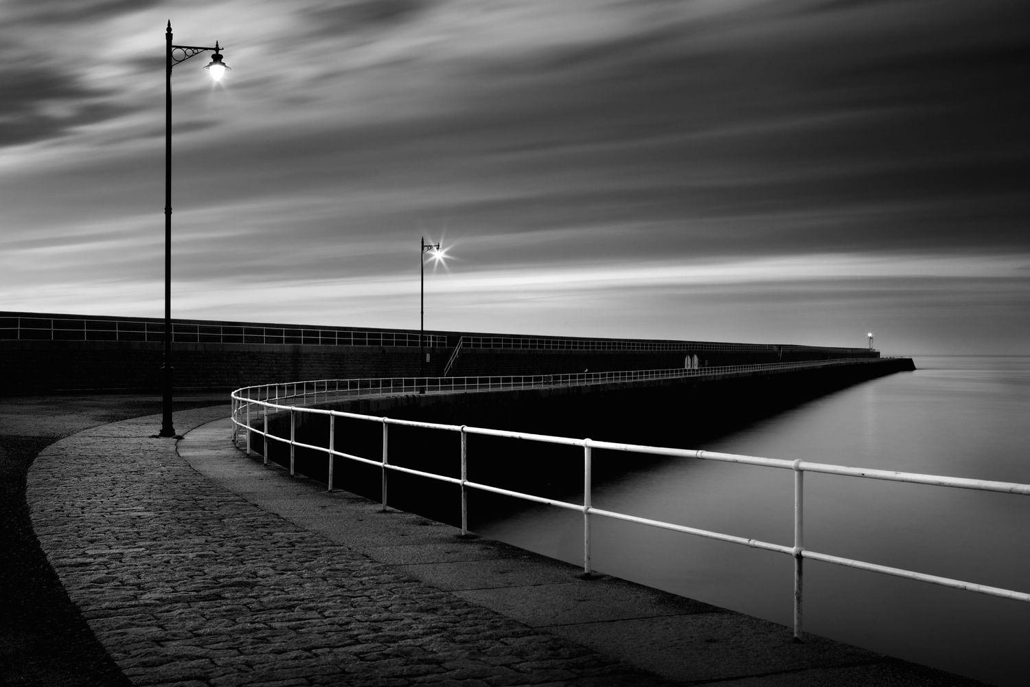 Minimalist black and white panorama of a pier railing extending into misty darkness.
