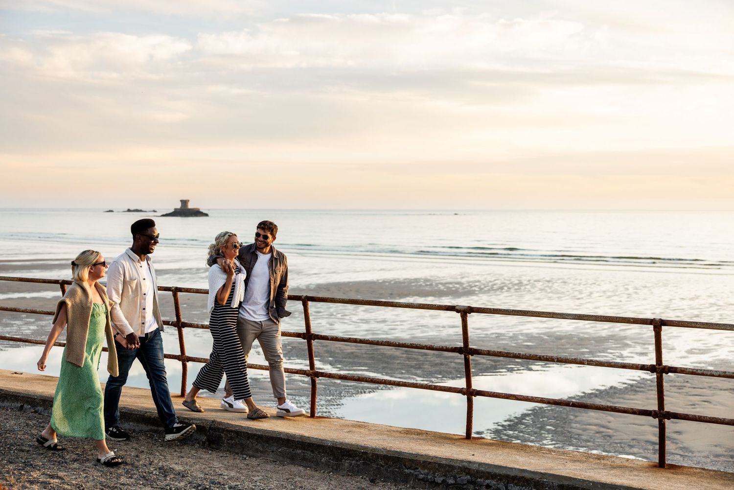 Sunset view of a wooden boardwalk along a sandy beach with people walking.