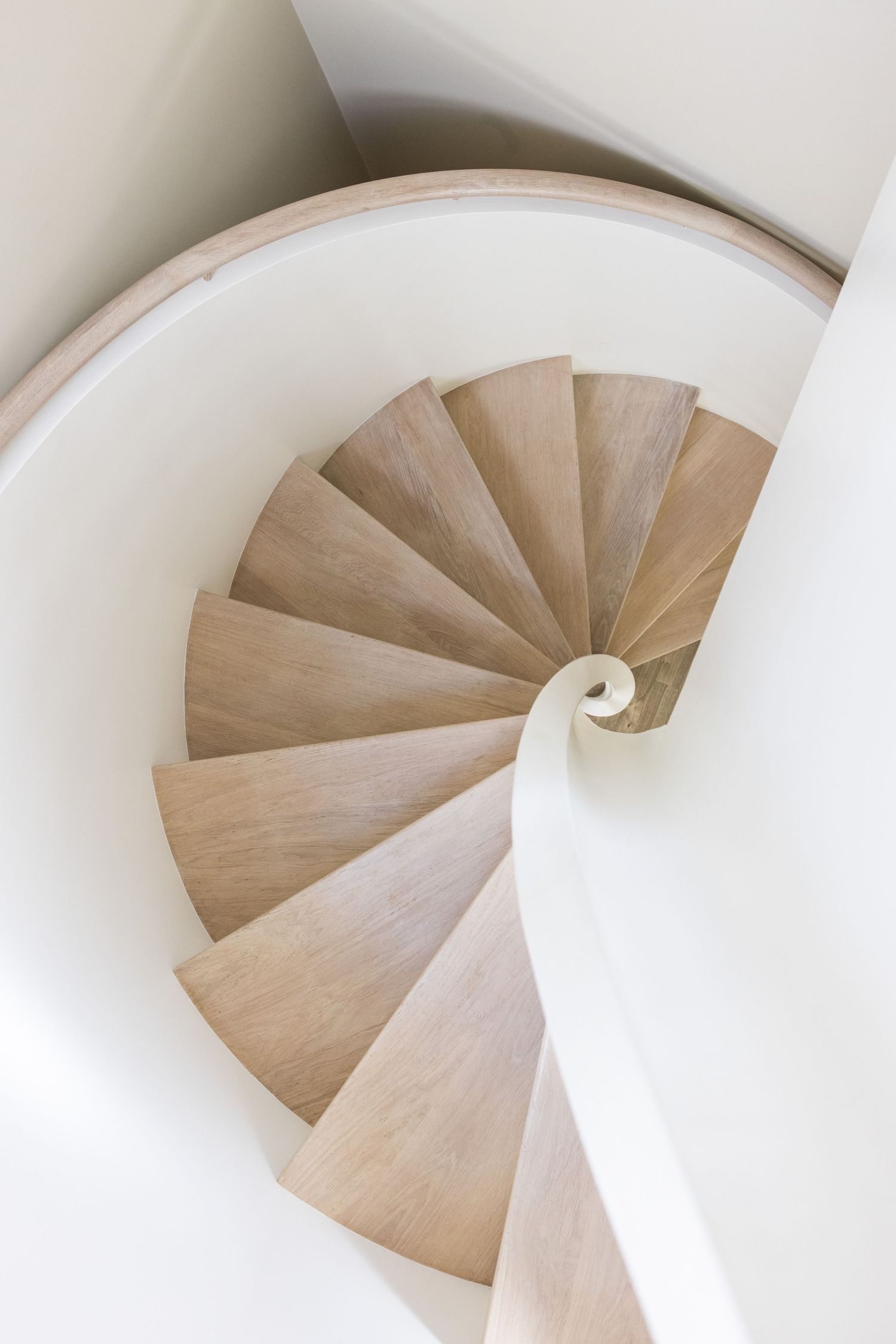 Minimalist spiral staircase with white walls and light wood steps creates elegant curves.