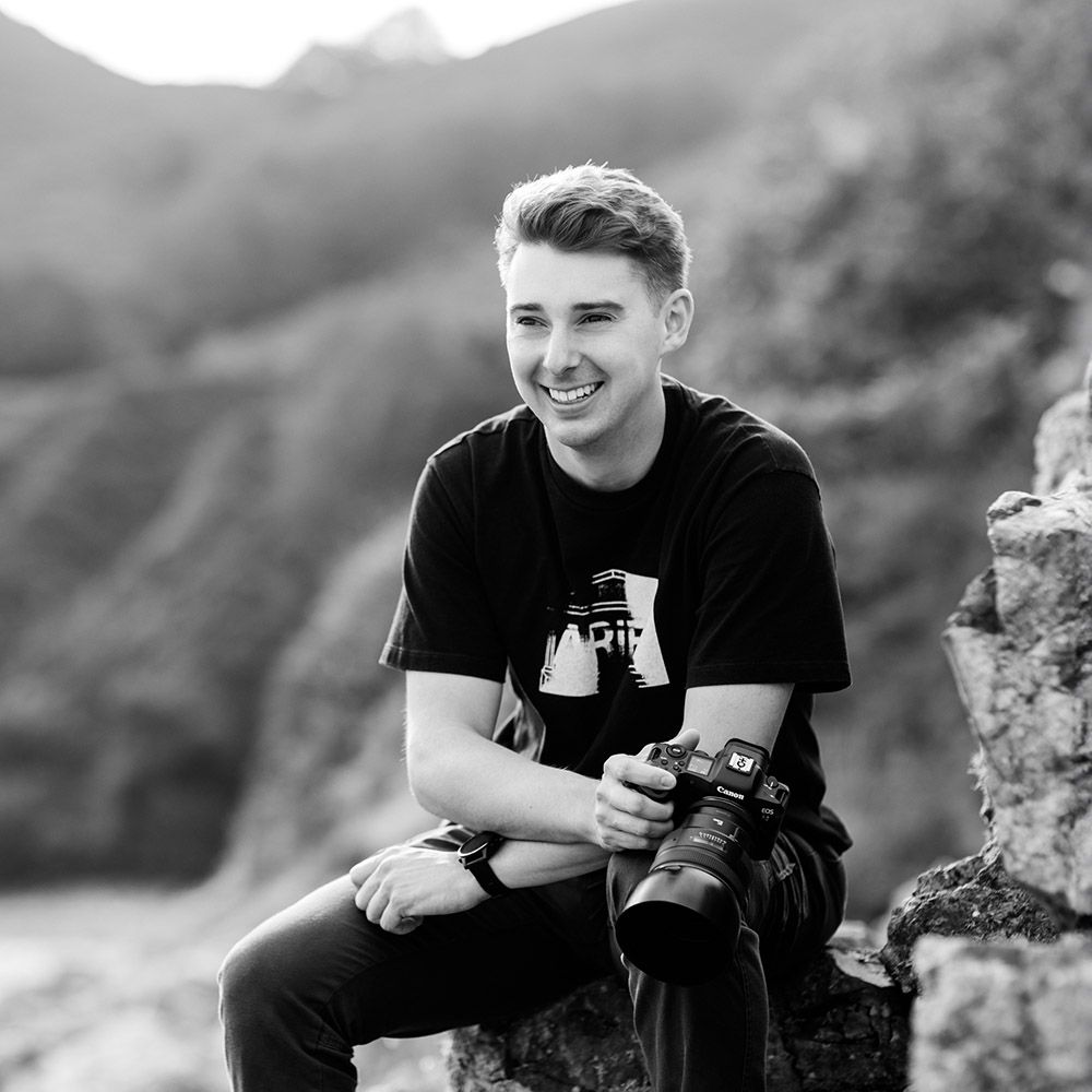 Black and white portrait of young photographer with camera in mountain setting.