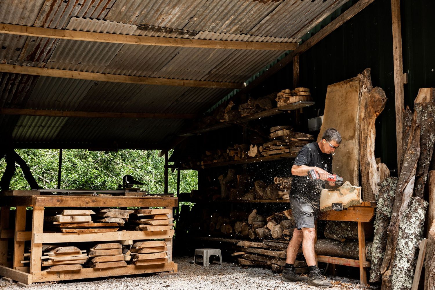 Wide view of covered outdoor workshop with stacked wood and work stations.