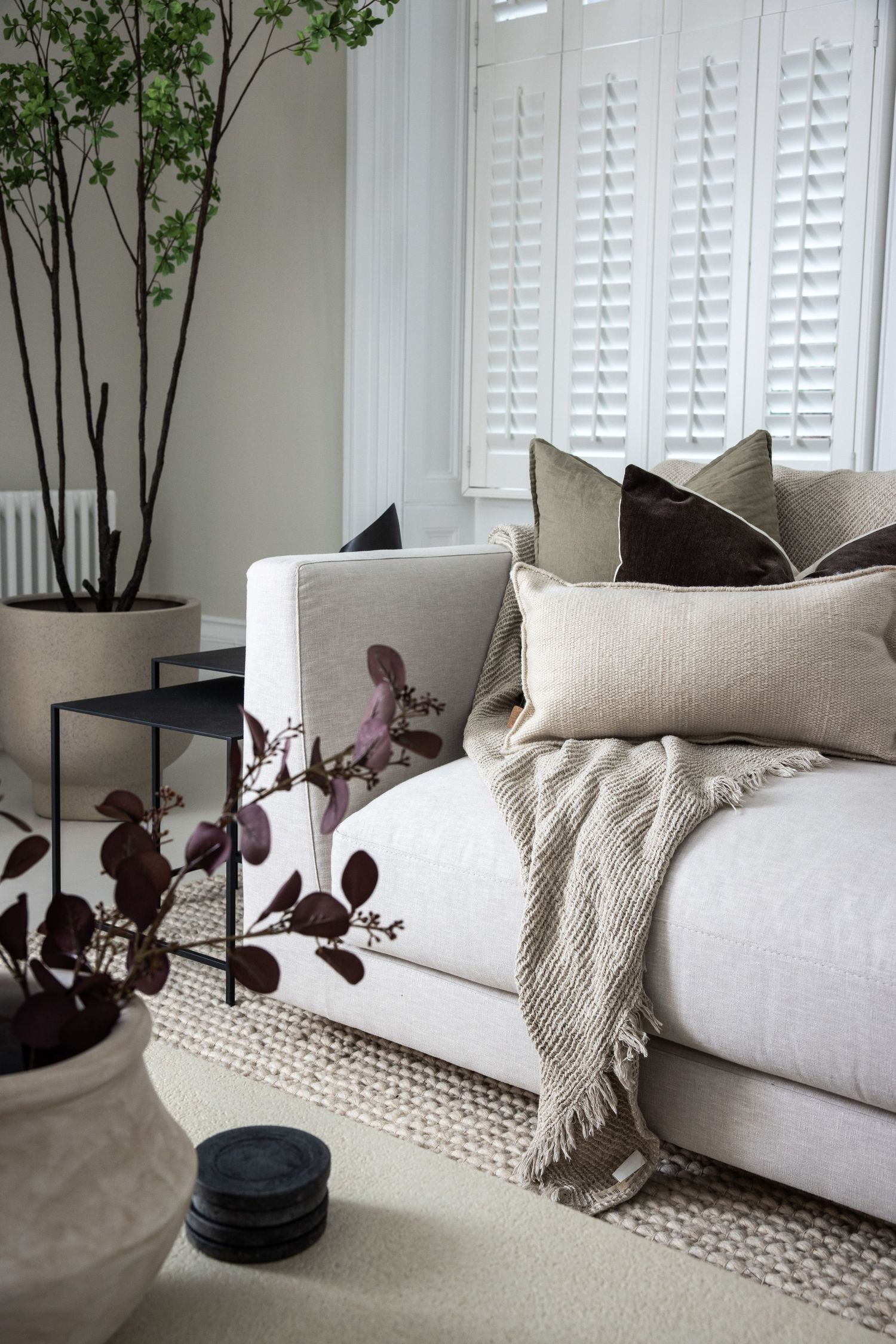 Cozy living room corner with white sofa, textured throw pillows and indoor plants.