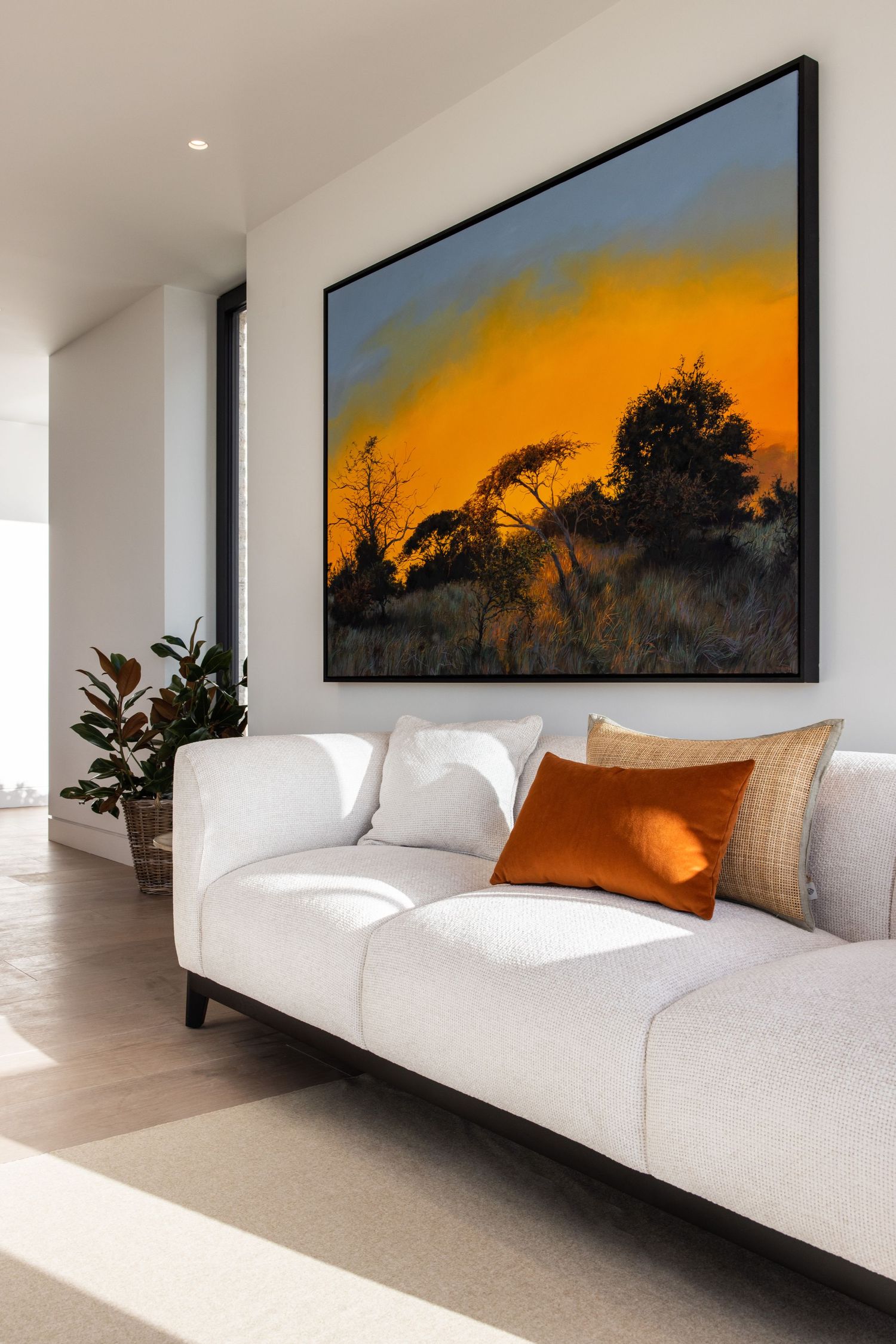 Close-up of modern white sofa with orange accent pillows beneath framed sunset artwork.