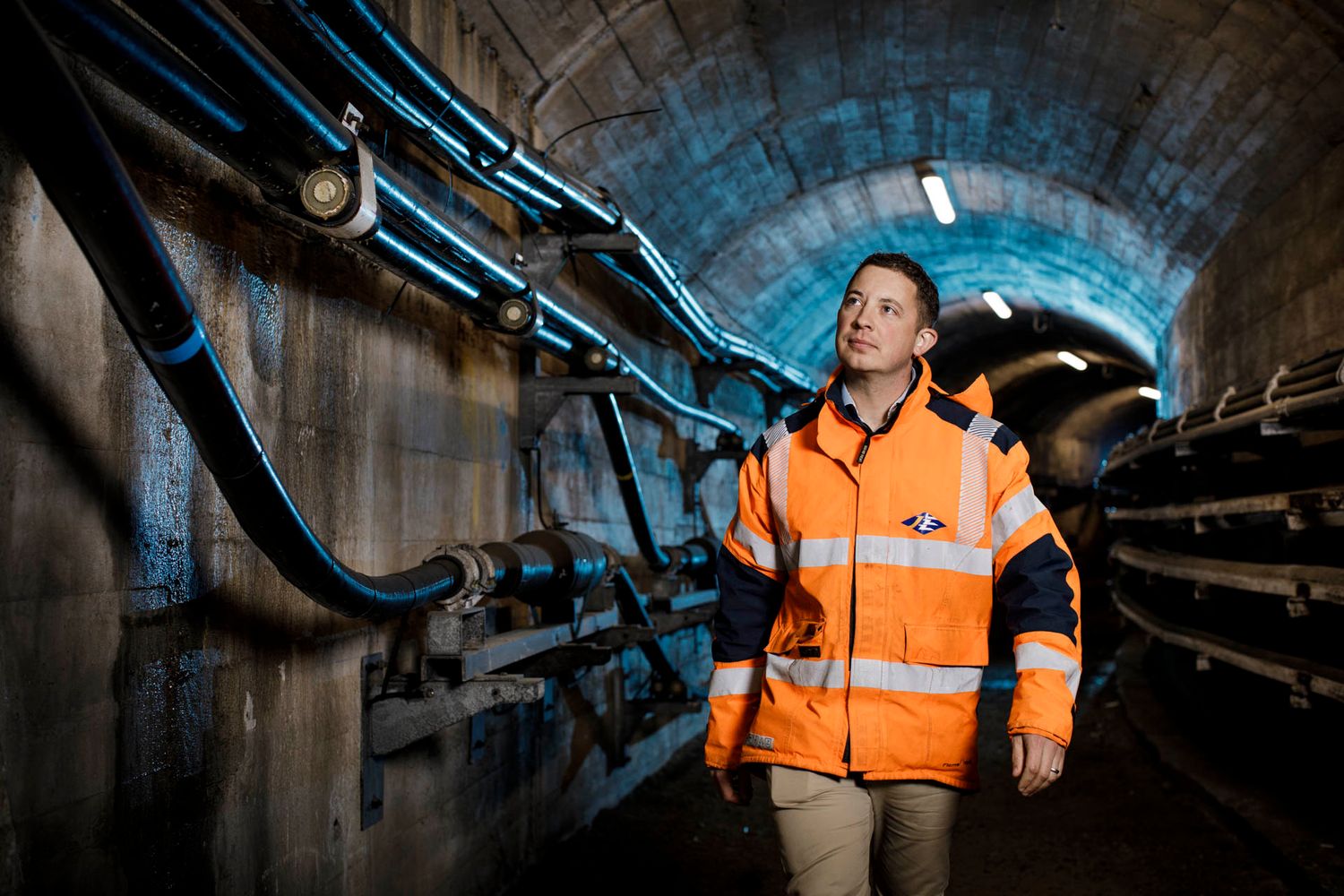 Worker in safety gear inspecting industrial tunnel infrastructure.