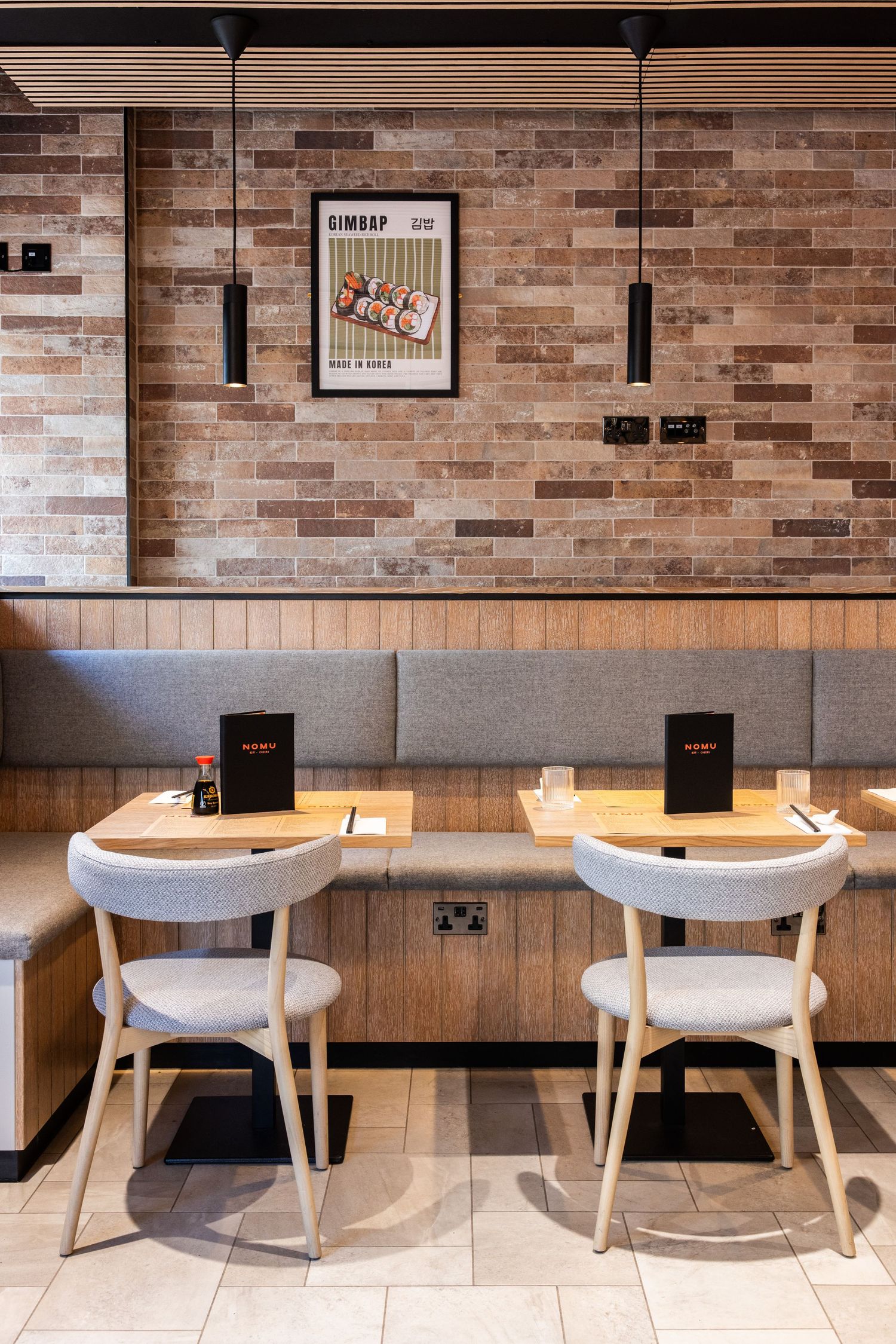 Modern cafe interior with brick walls, pendant lights, and white chairs at wooden counter seating.