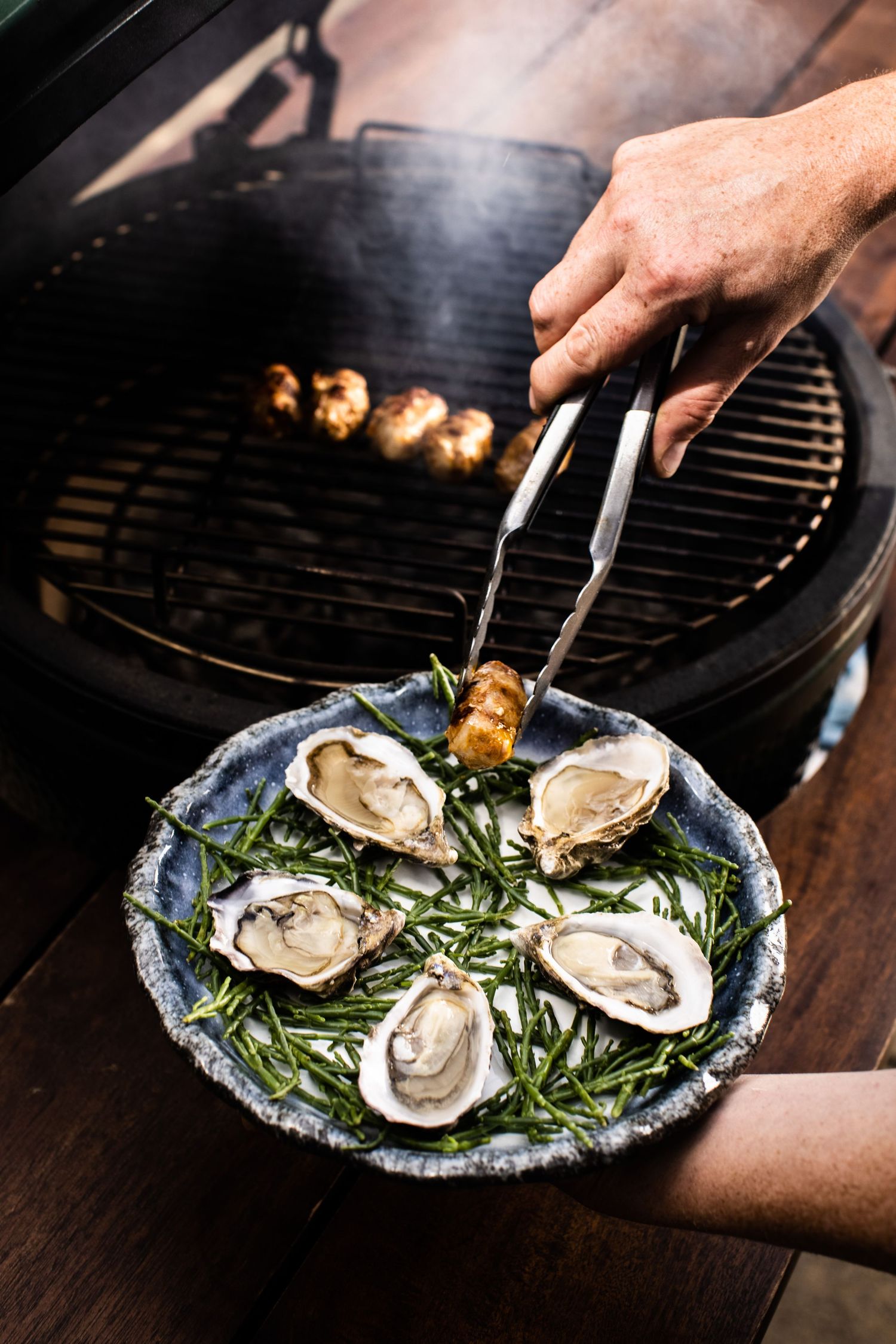 Fresh oysters being prepared on bed of seaweed on decorative blue plate.