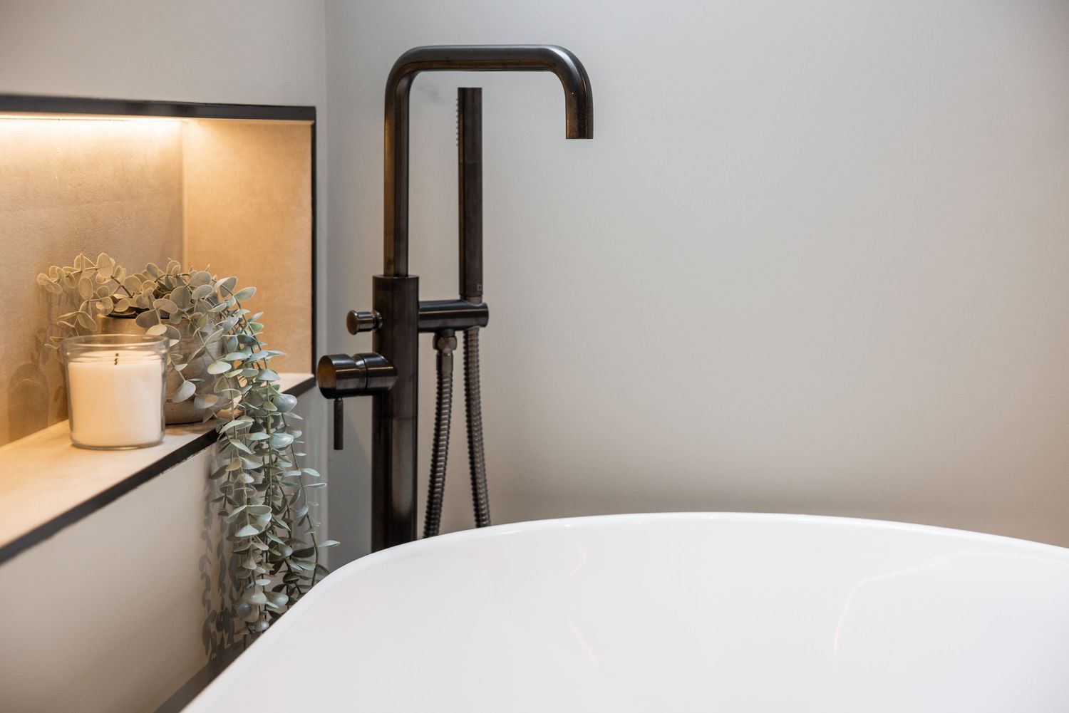 Freestanding bathtub with matte black faucet and dried floral decor in modern bathroom.