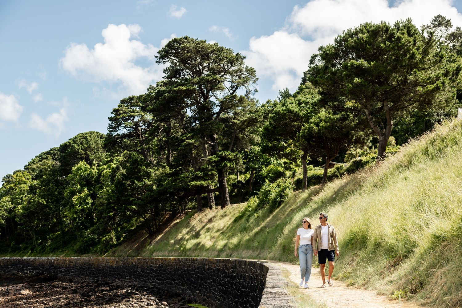 People walking along grassy hillside path on sunny summer day.