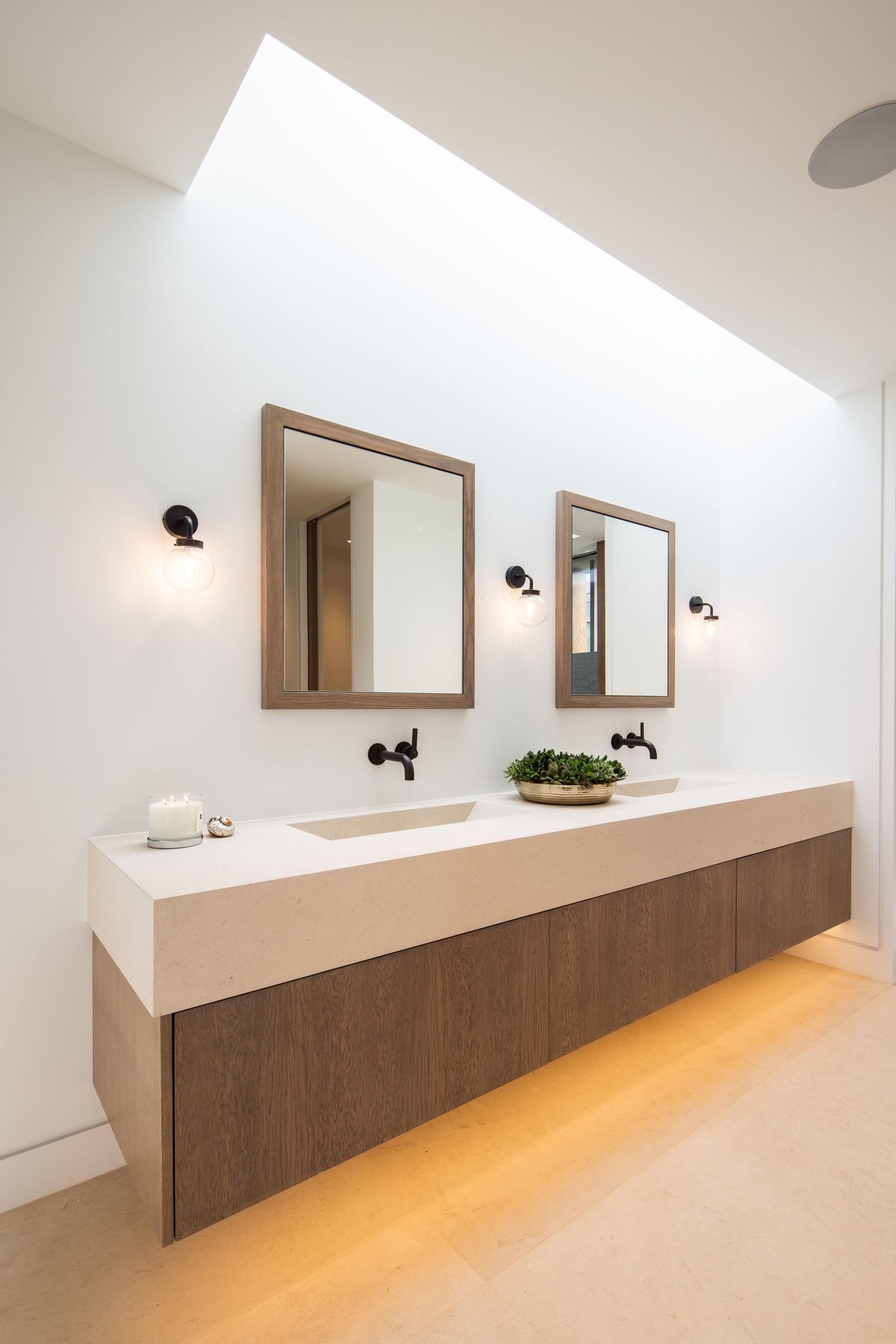 Minimalist bathroom vanity with floating wooden cabinets and dual mirrors under skylight.