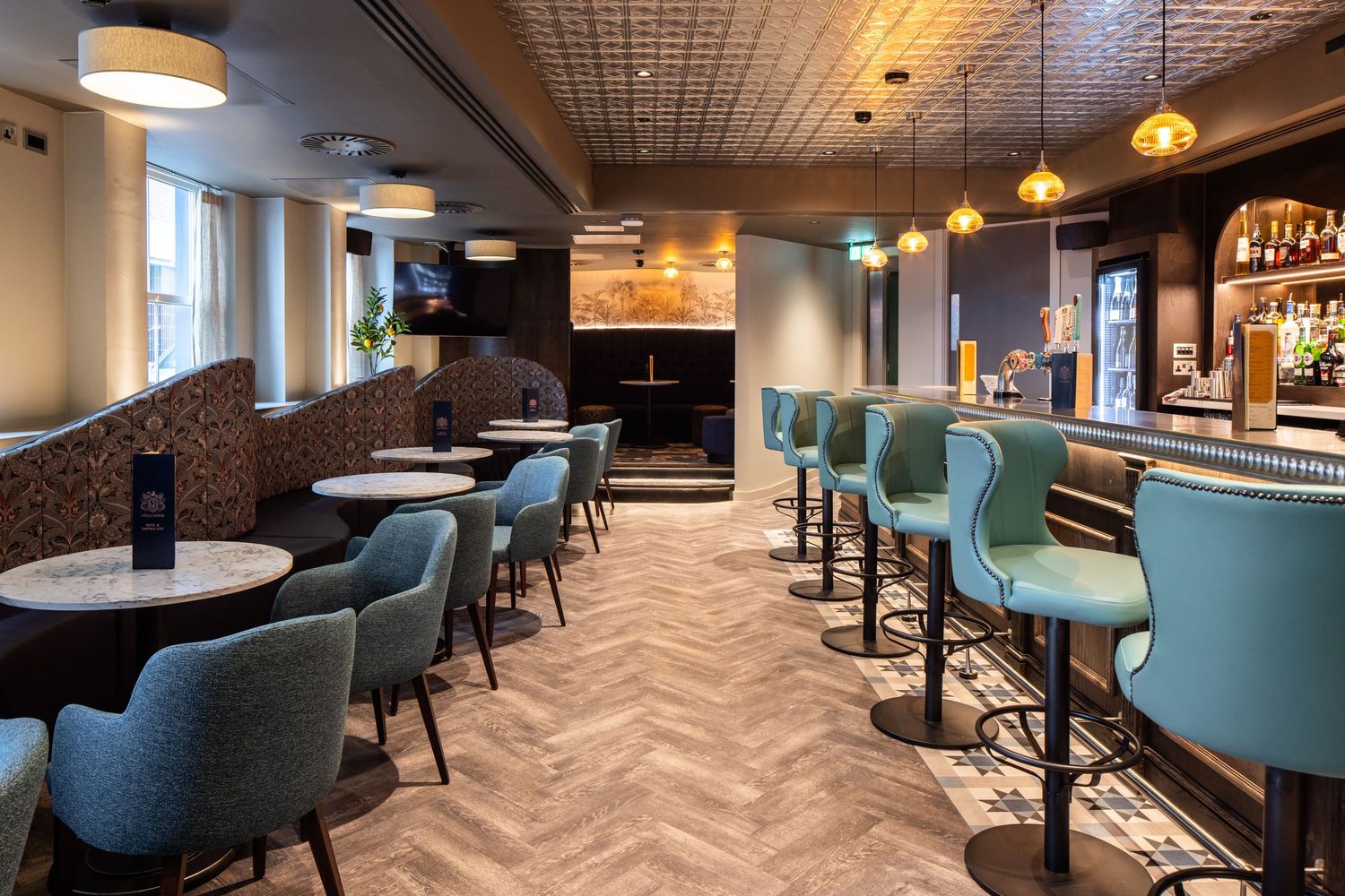 Modern restaurant interior with teal upholstered chairs and herringbone flooring creates an elegant dining atmosphere.