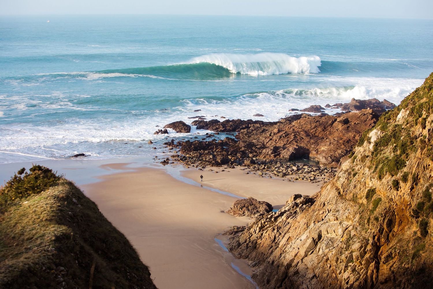 Coastal landscape with rocky cliffs and breaking waves along a sandy beach.