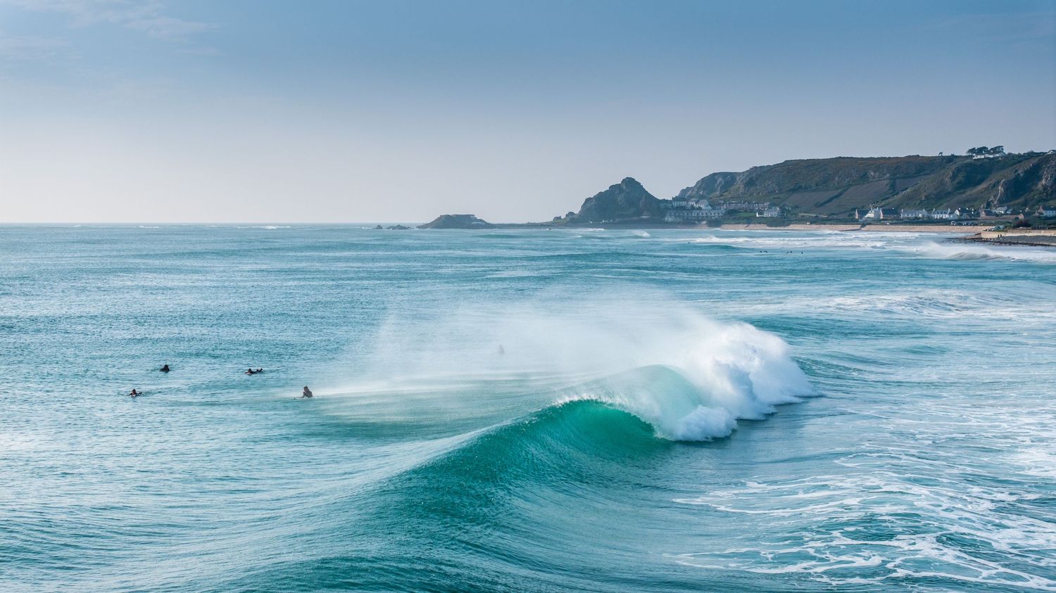 Pristine turquoise waves rolling across a wide ocean panorama under clear blue skies.