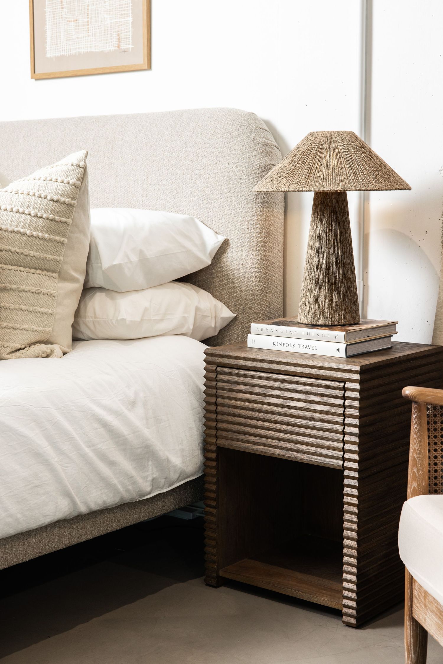 Cozy bedroom corner with textured bedding, striped nightstand and natural fiber table lamp.